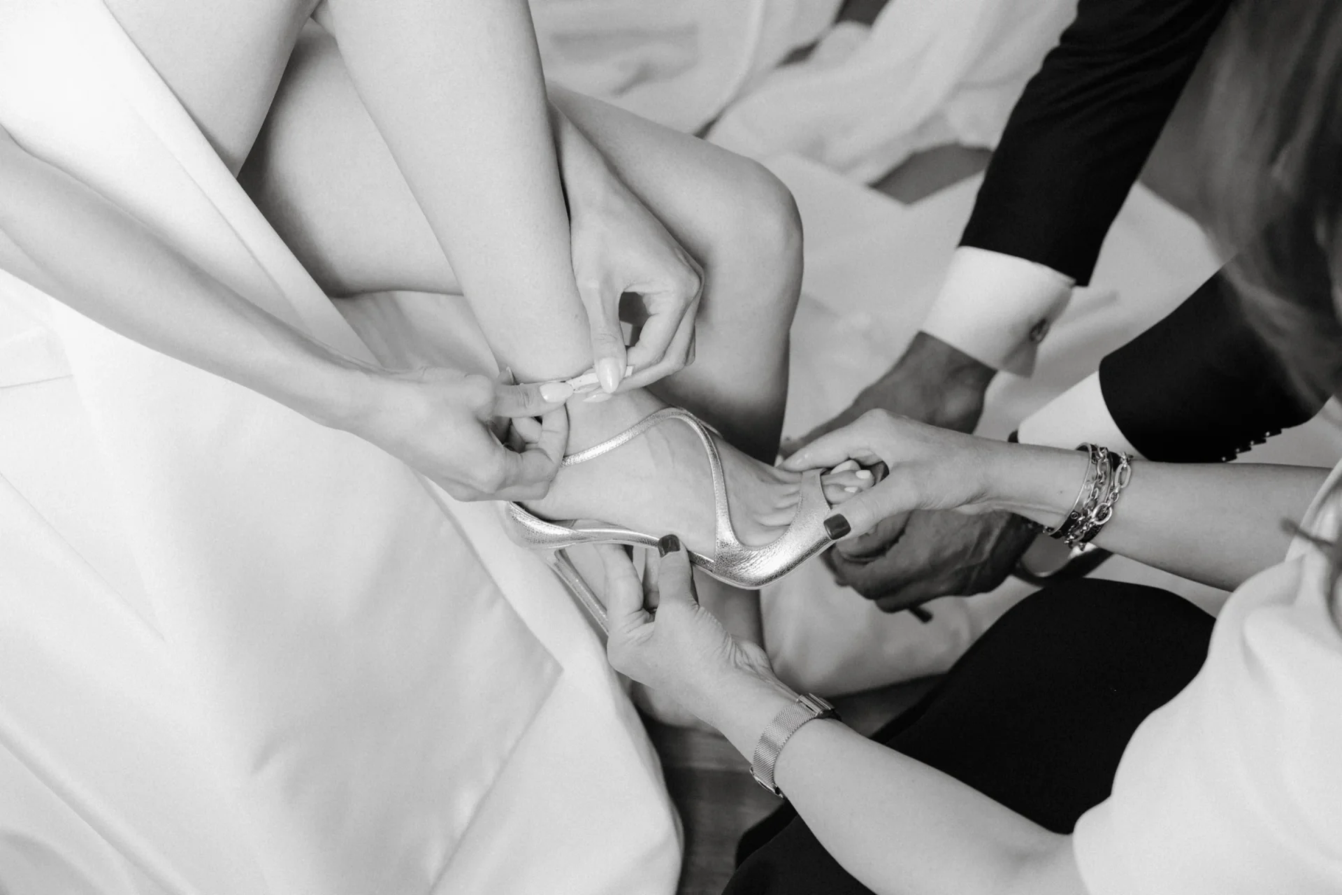 Black and white close-up of hands helping fasten the bride's shoe