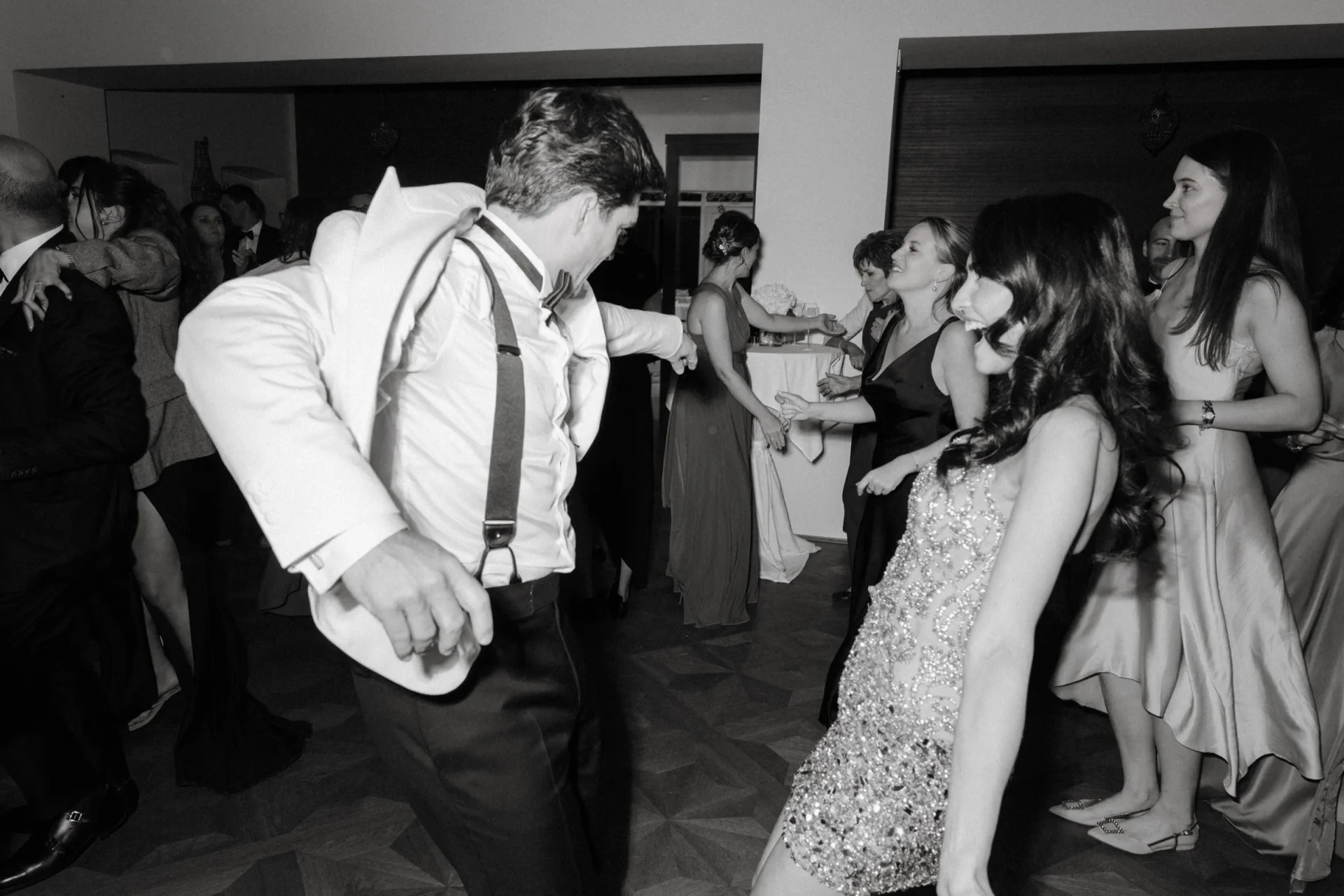 Groom in suspenders dancing with the bride and guests, black and white