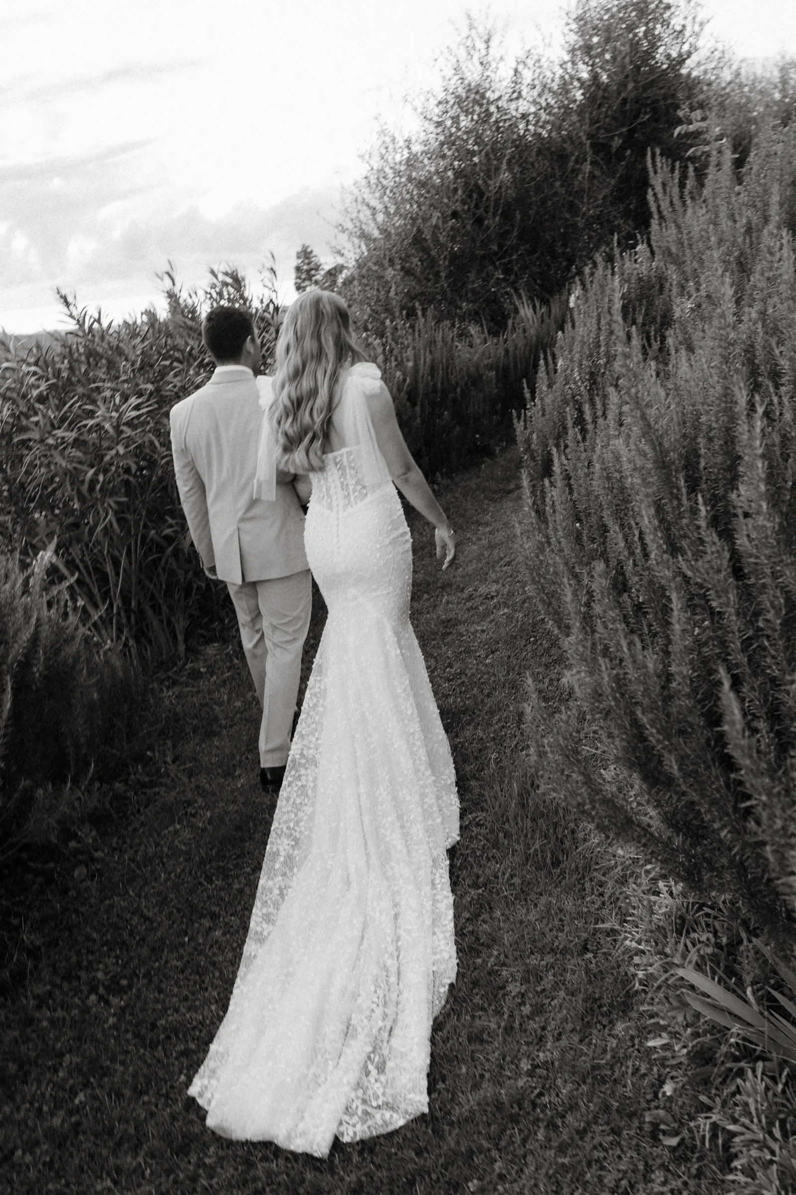 Black and white: the bride's lace train trailing behind her on the garden path