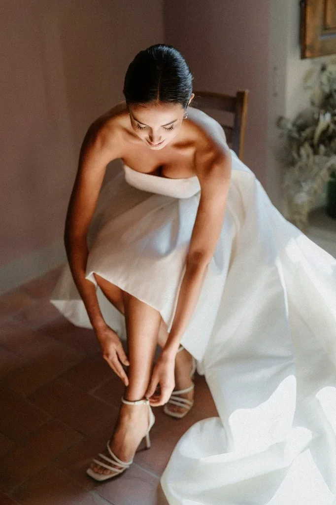 Bride buckling her sandal in warm light on a terracotta floor