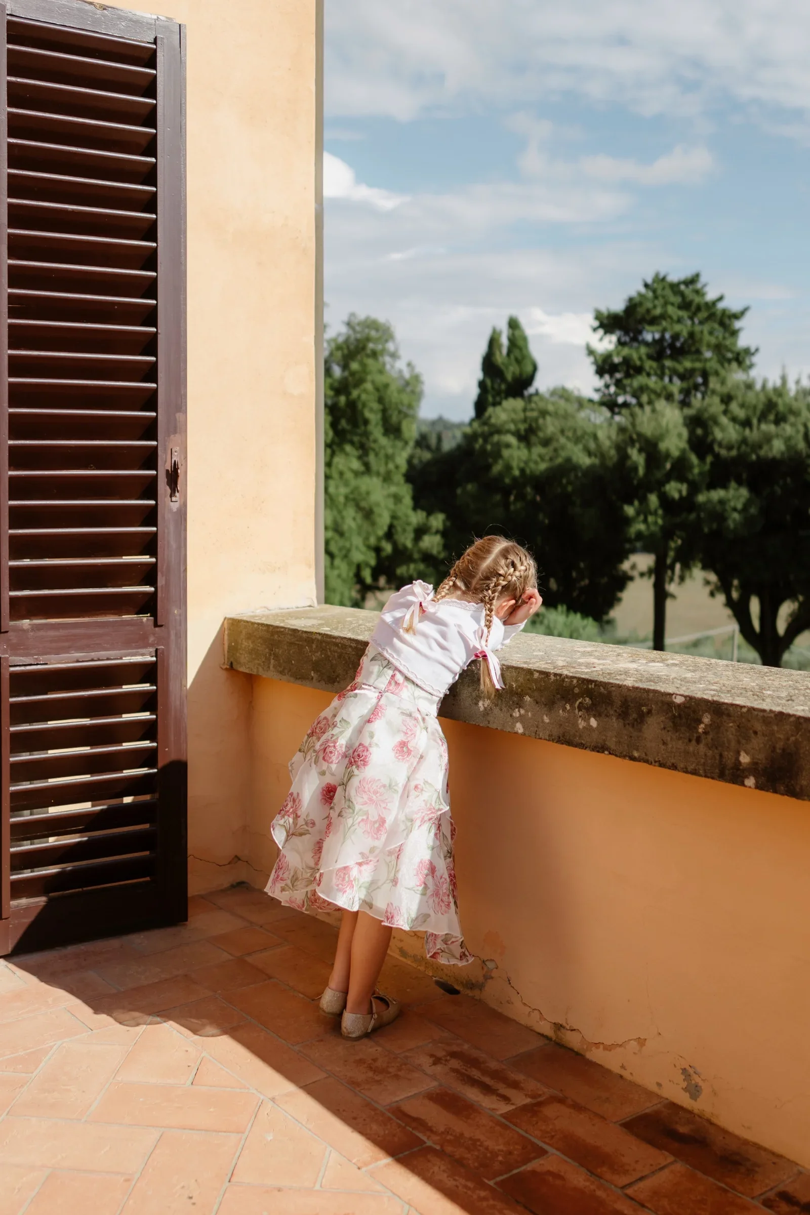 A flower girl in a printed dress leaning over the villa's balcony wall