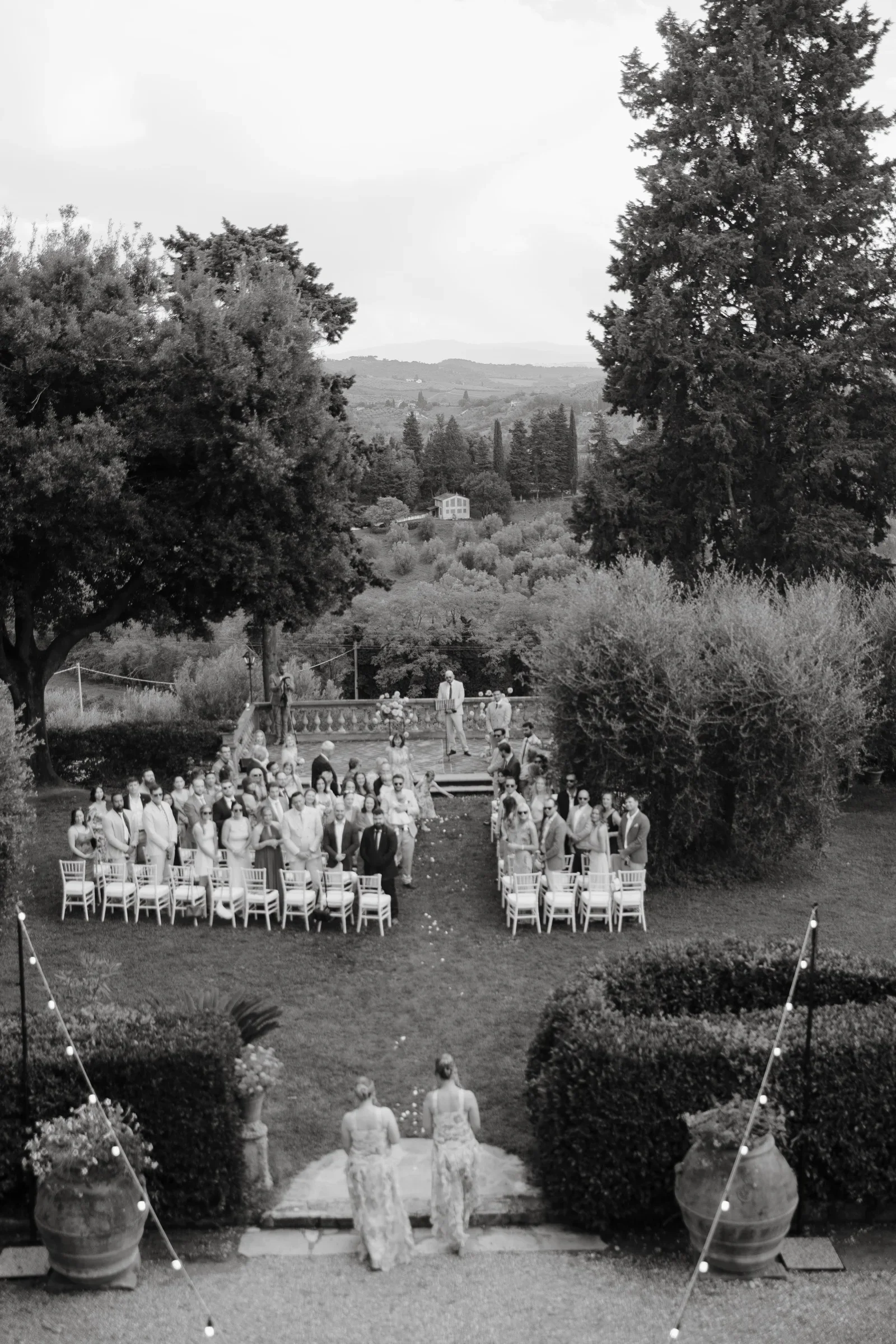 Black and white overhead view of the ceremony: white chairs in the walled garden, hills beyond