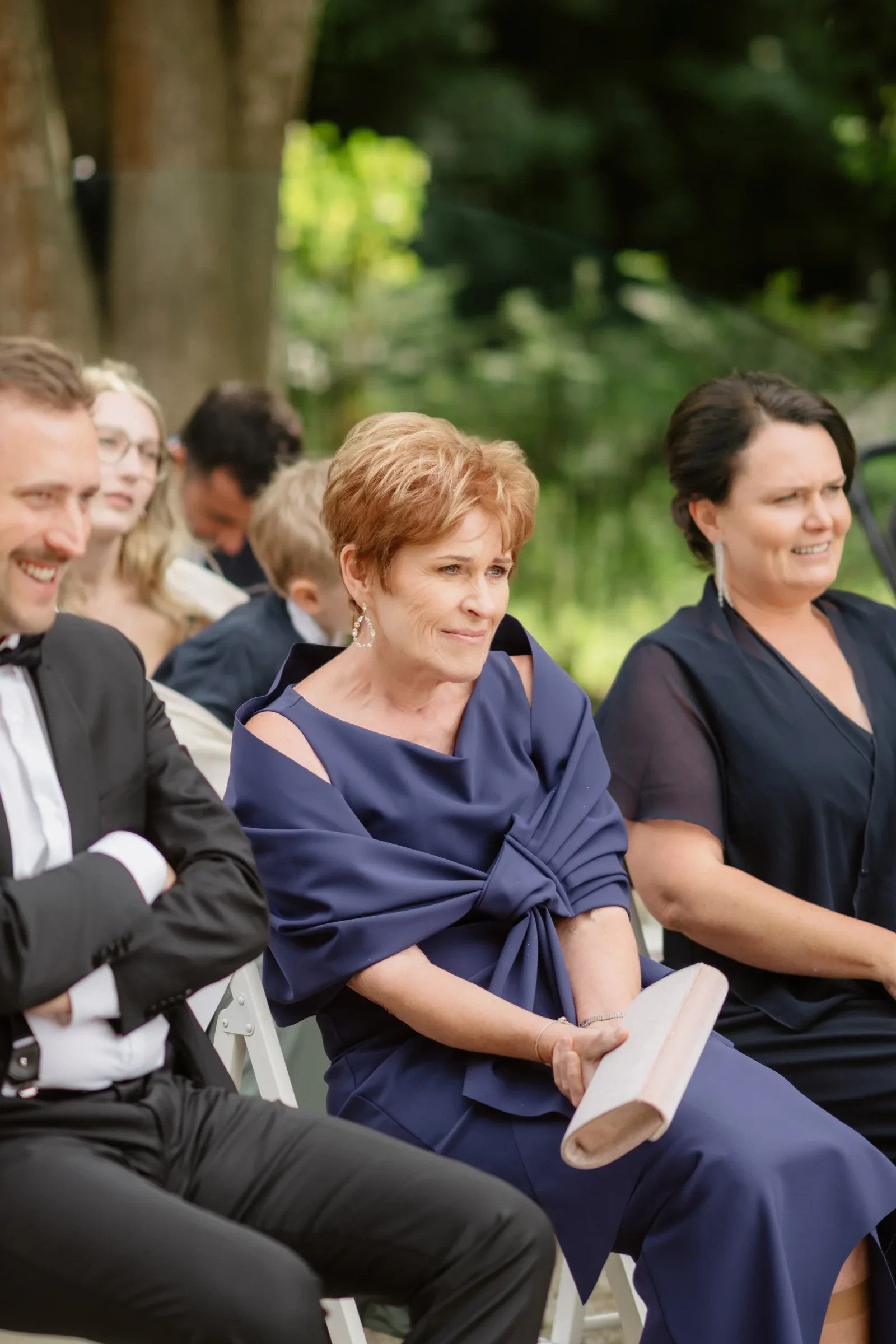 Guests seated at the ceremony, a woman in a navy dress holding a program