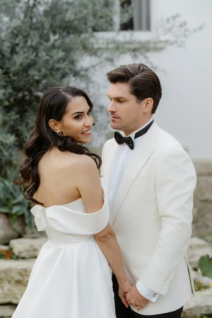 Newlyweds glancing back over their shoulders beside an olive tree