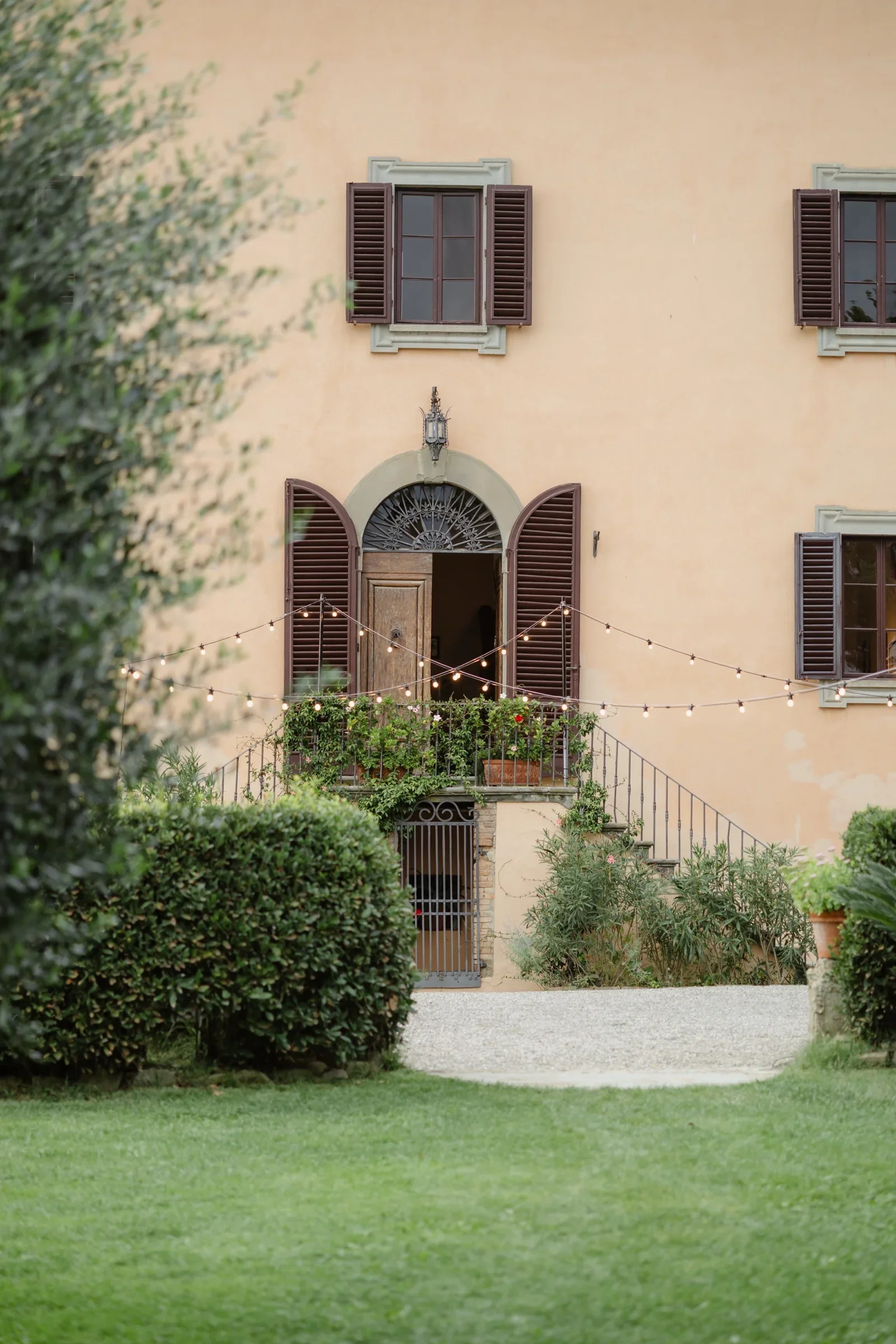 The villa's pink facade behind a clipped lawn, festoon lights waiting for the evening
