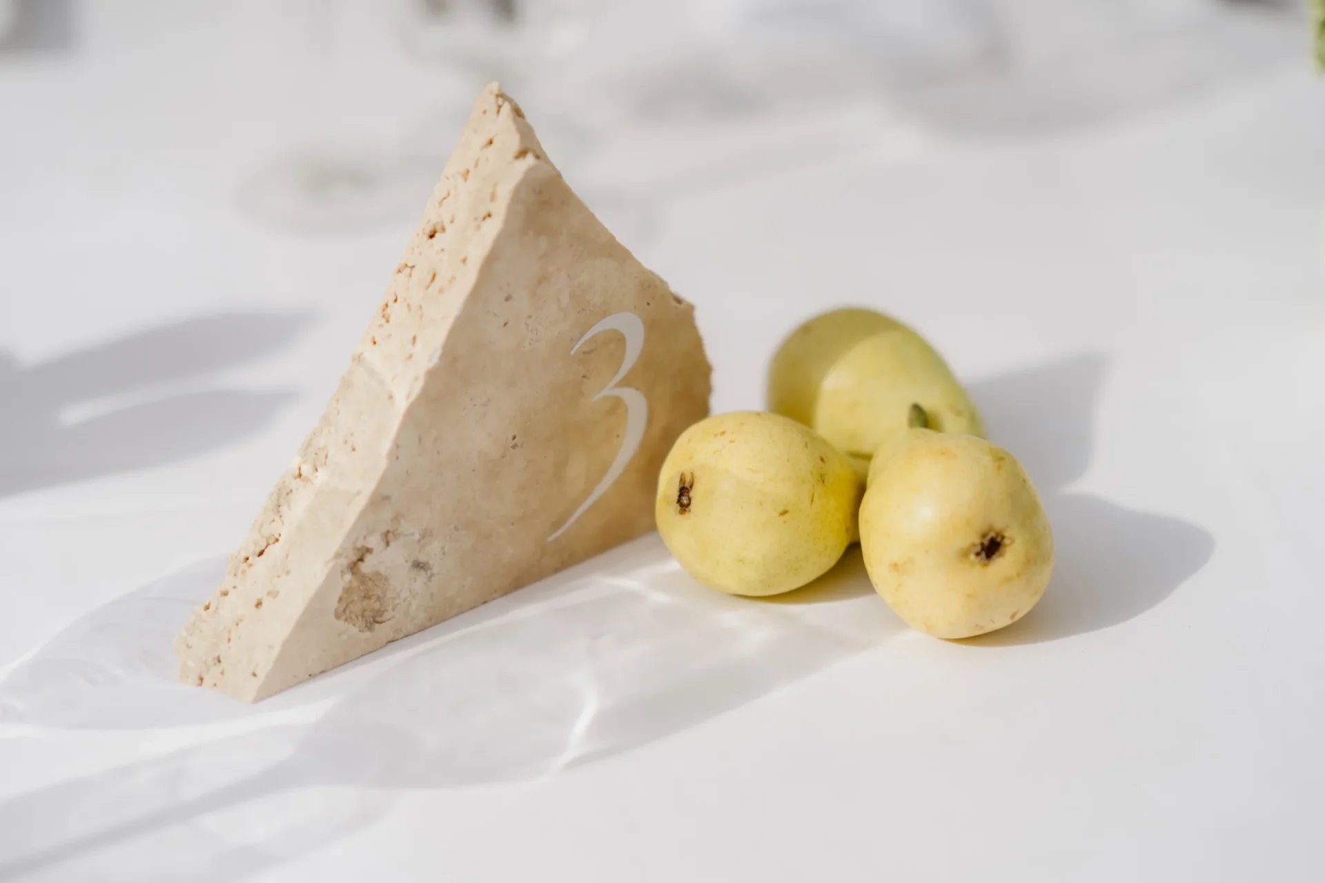 Wedge of cheese and three yellow pears on a white tablecloth