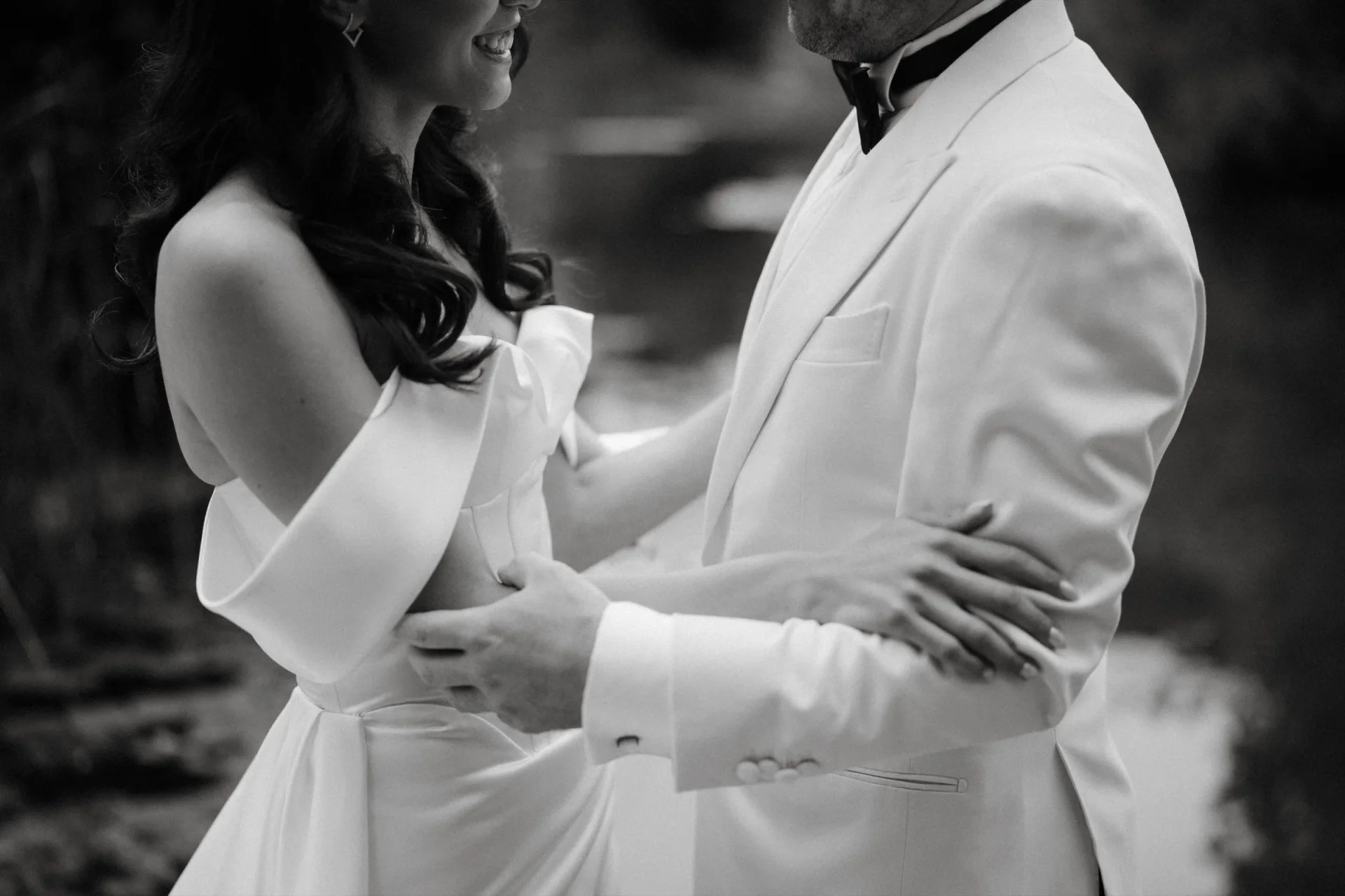 Black and white close-up of the couple embracing, the groom in a white dinner jacket