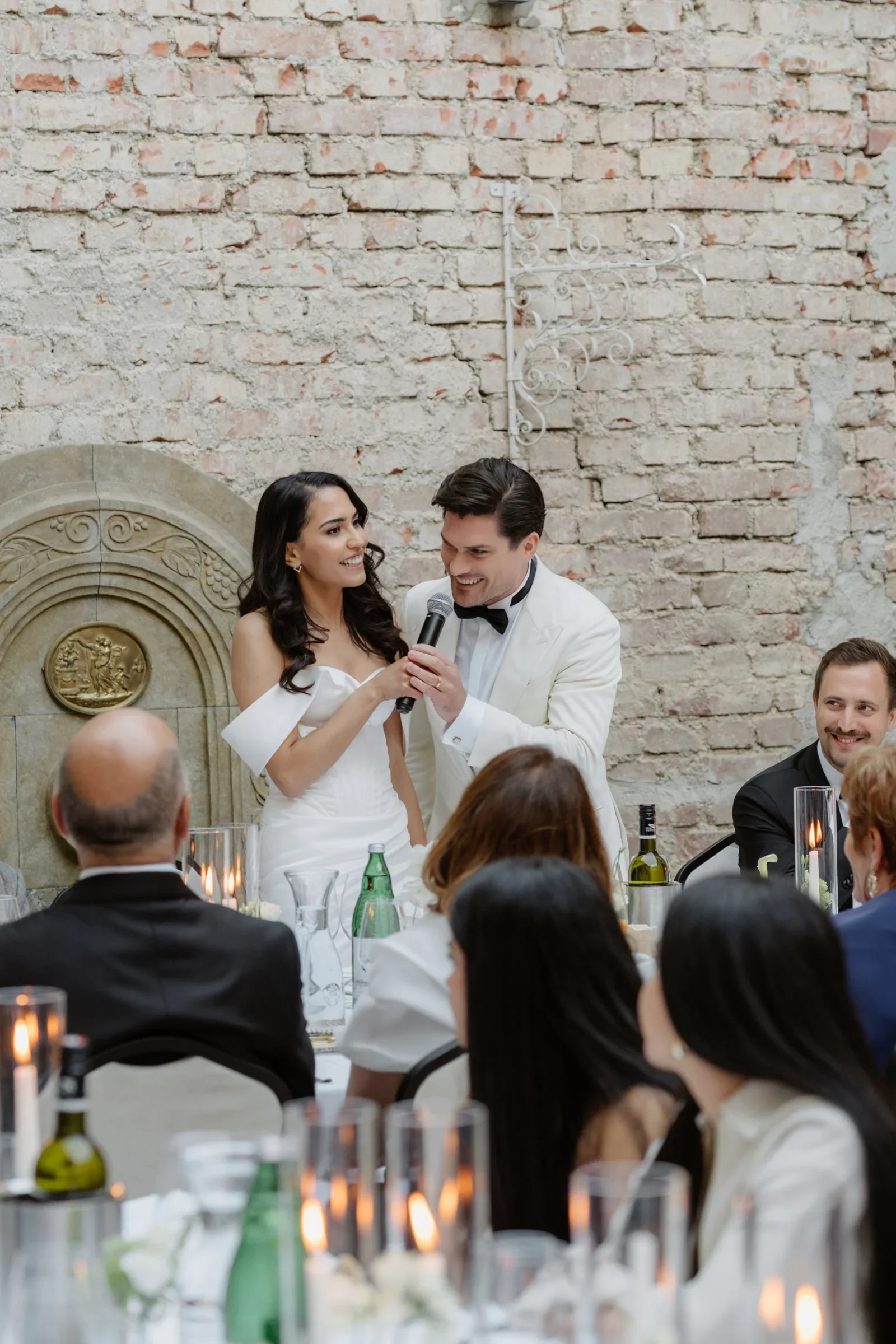 Bride and groom giving a speech at the dinner in front of a brick wall