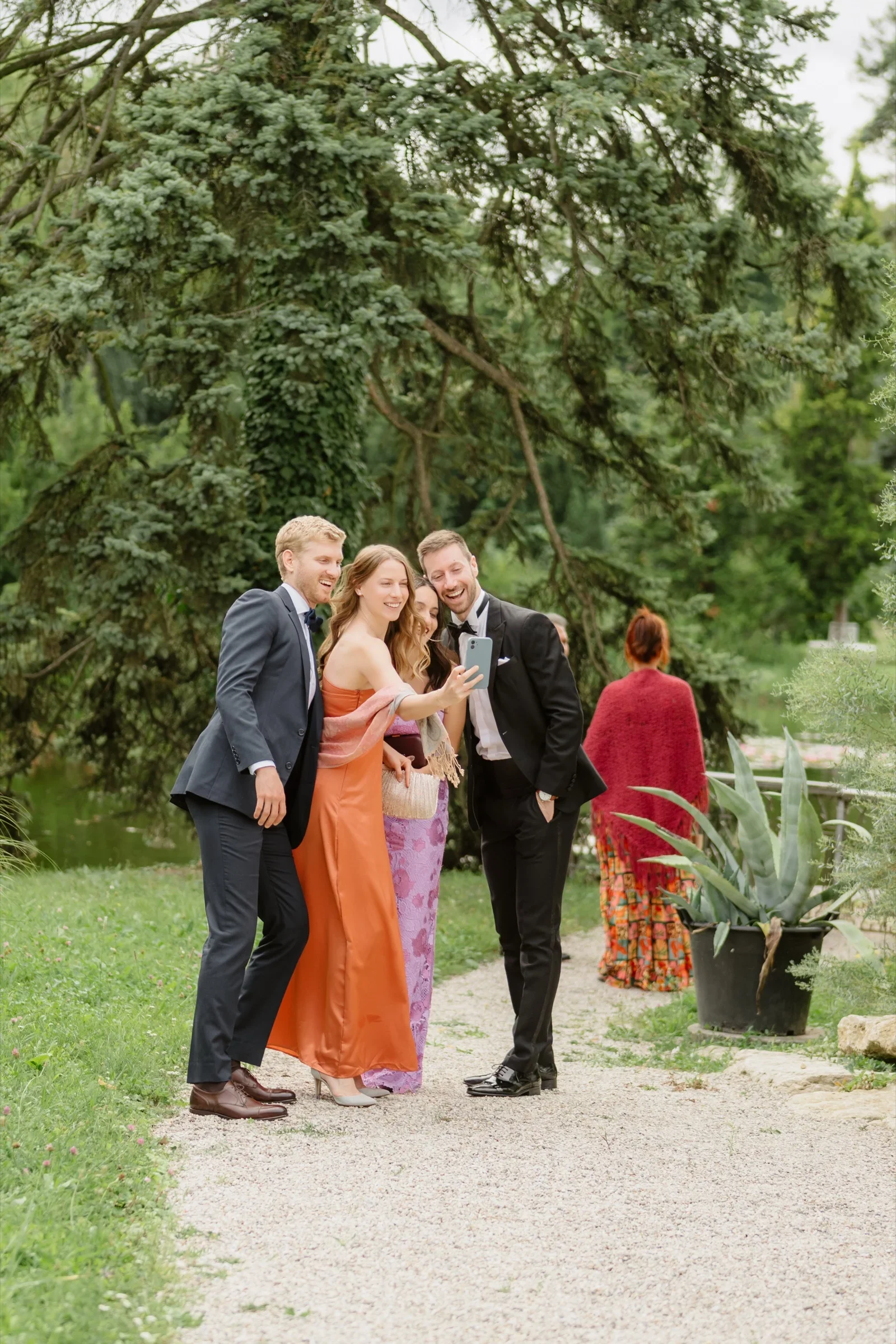 Wedding guests chatting on a garden path under tall trees