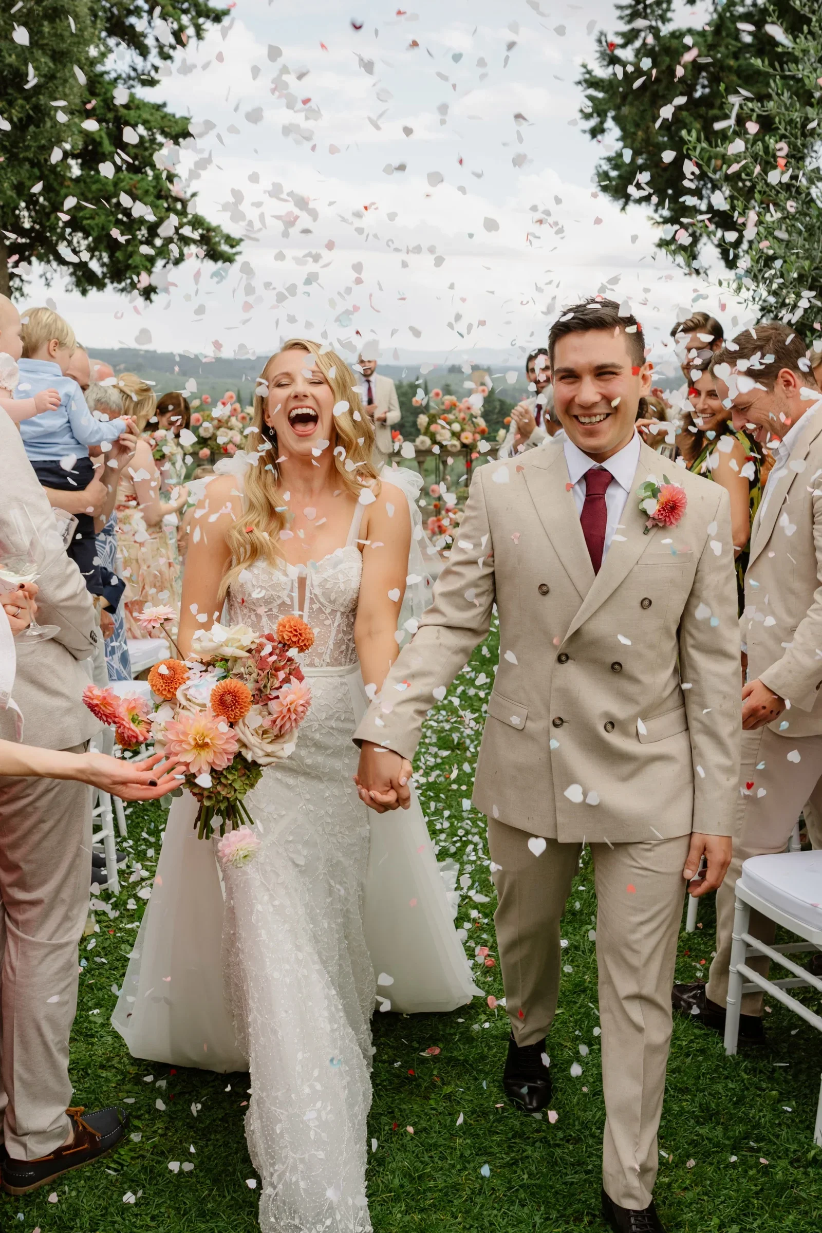 Lyndsey and Dom walking hand in hand through a shower of confetti after their ceremony at Villa Il Pozzo