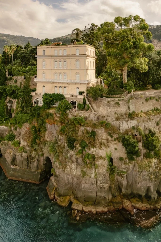 Pale villa perched on a cliff above turquoise coastal water