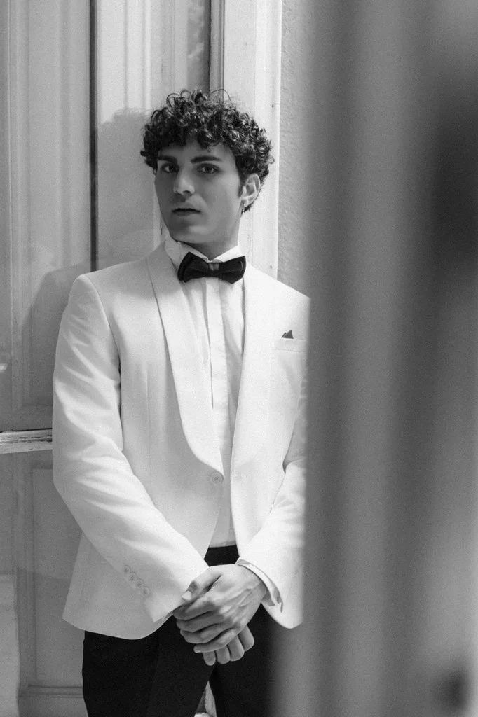 Groom in a white dinner jacket waiting beside a tall doorway