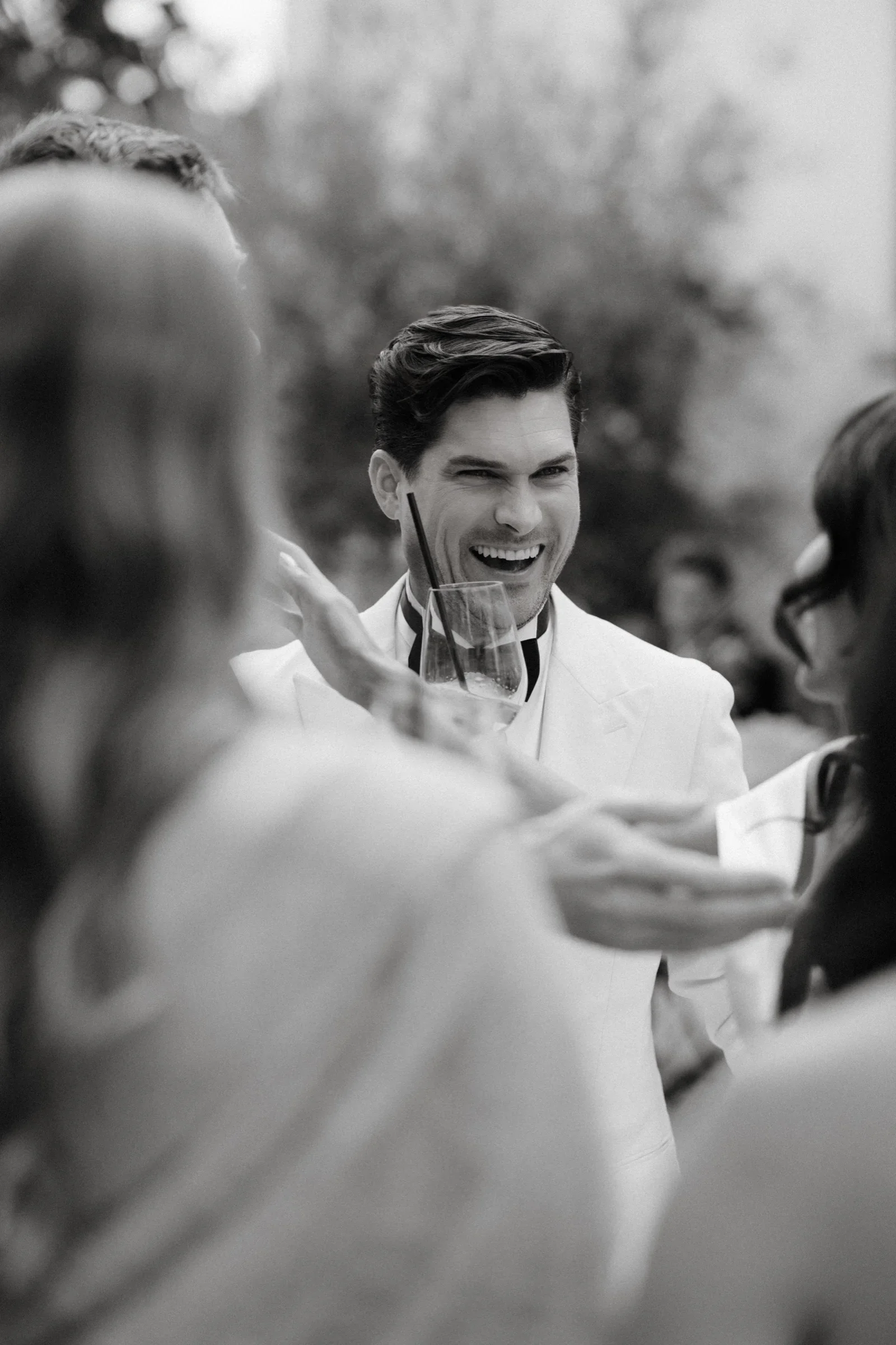Black and white photo of the groom laughing with guests around him