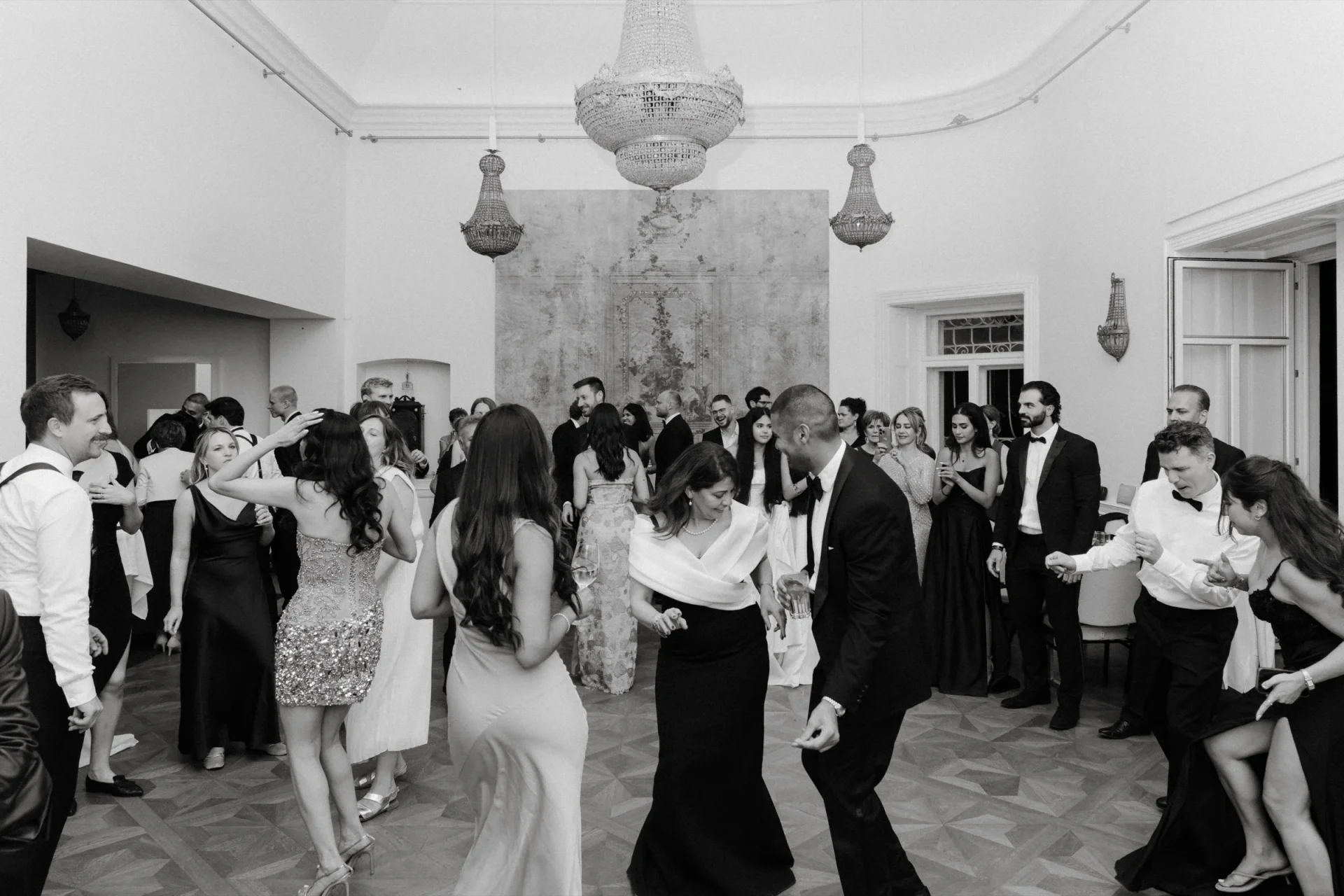 Crowded dance floor in a chandelier-lit hall, black and white