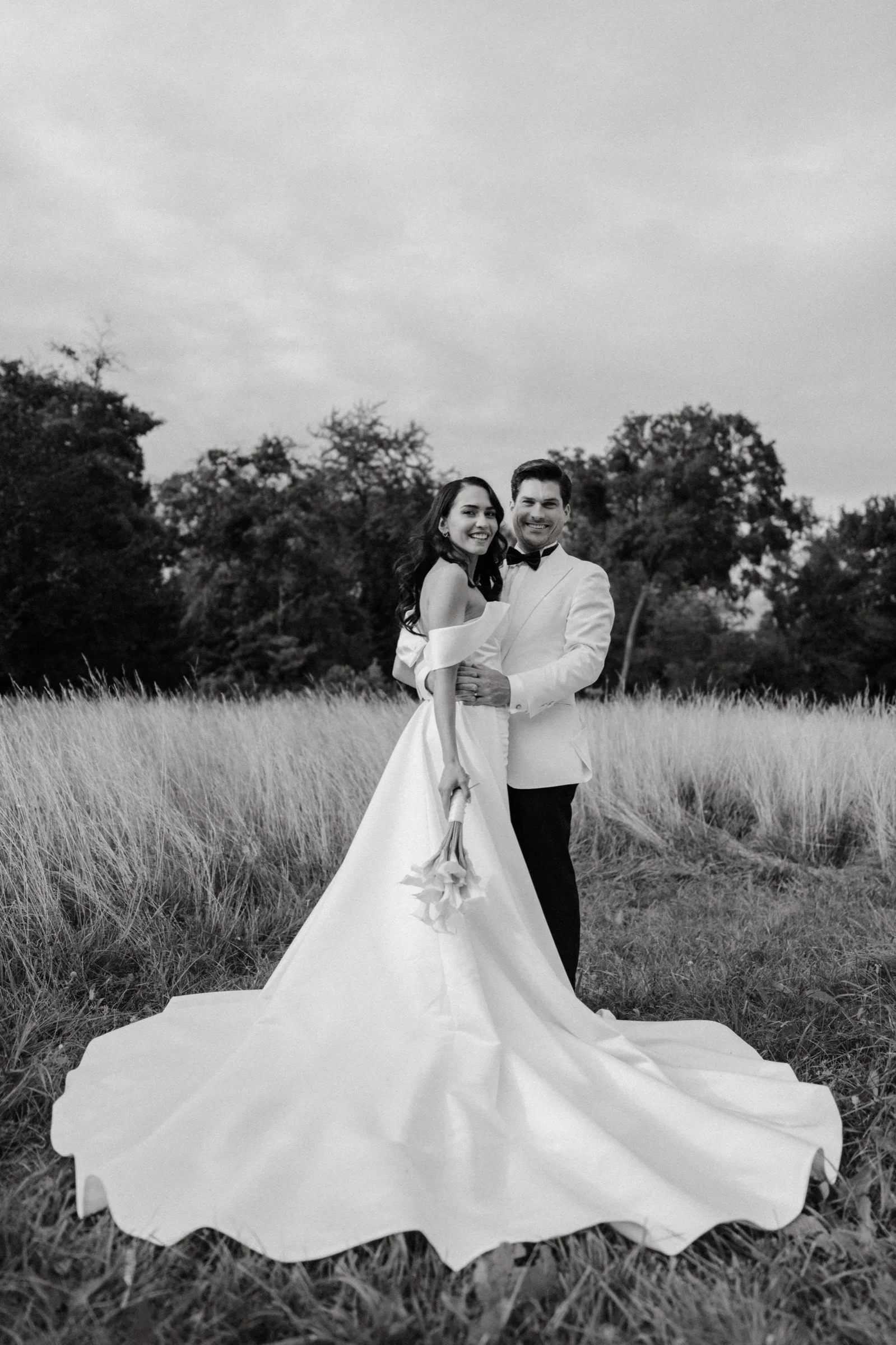 Couple in tall grass with the bride's long train spread out, black and white
