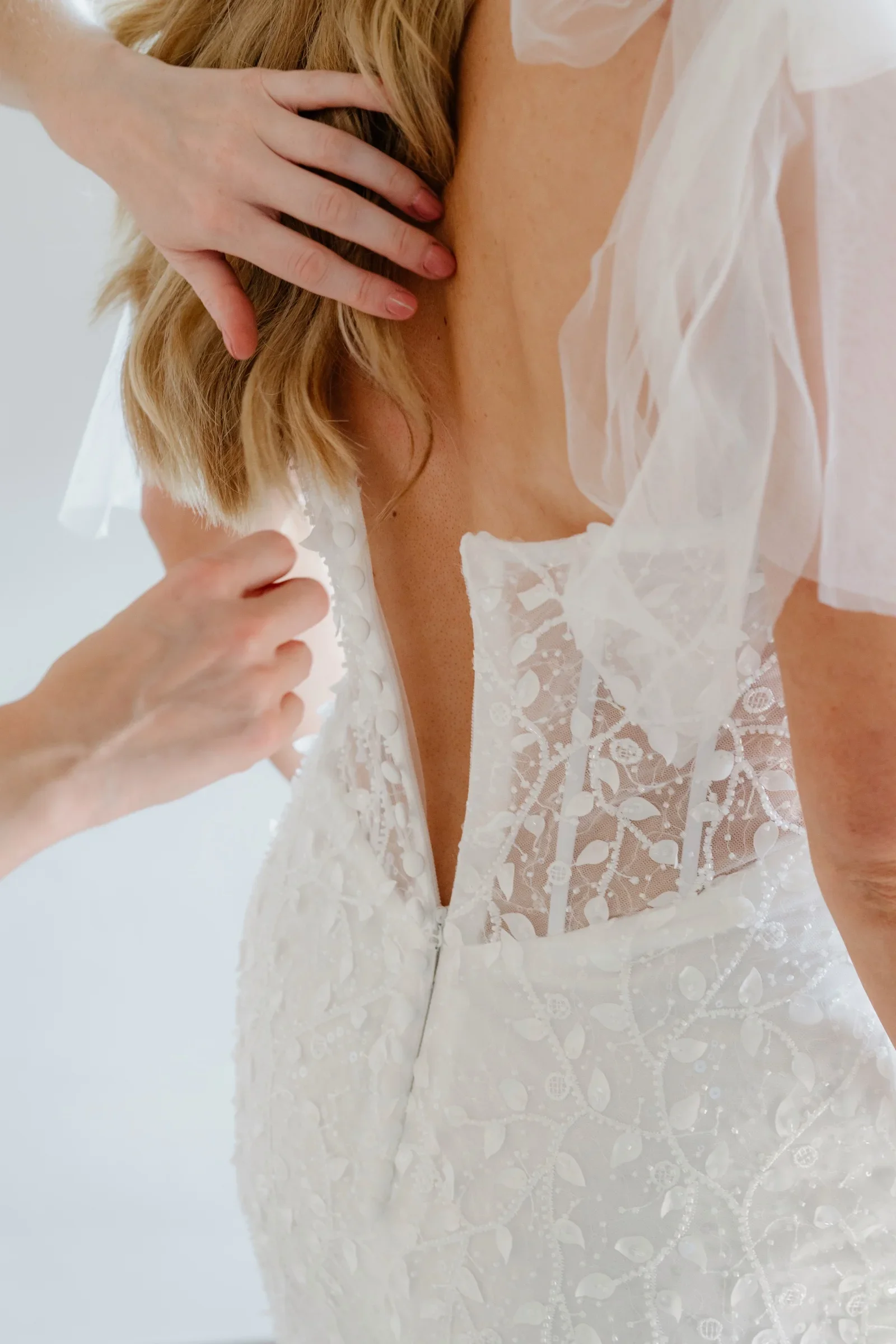 Close view of the bride's hand at the open lace back of her gown, veil falling over her shoulder