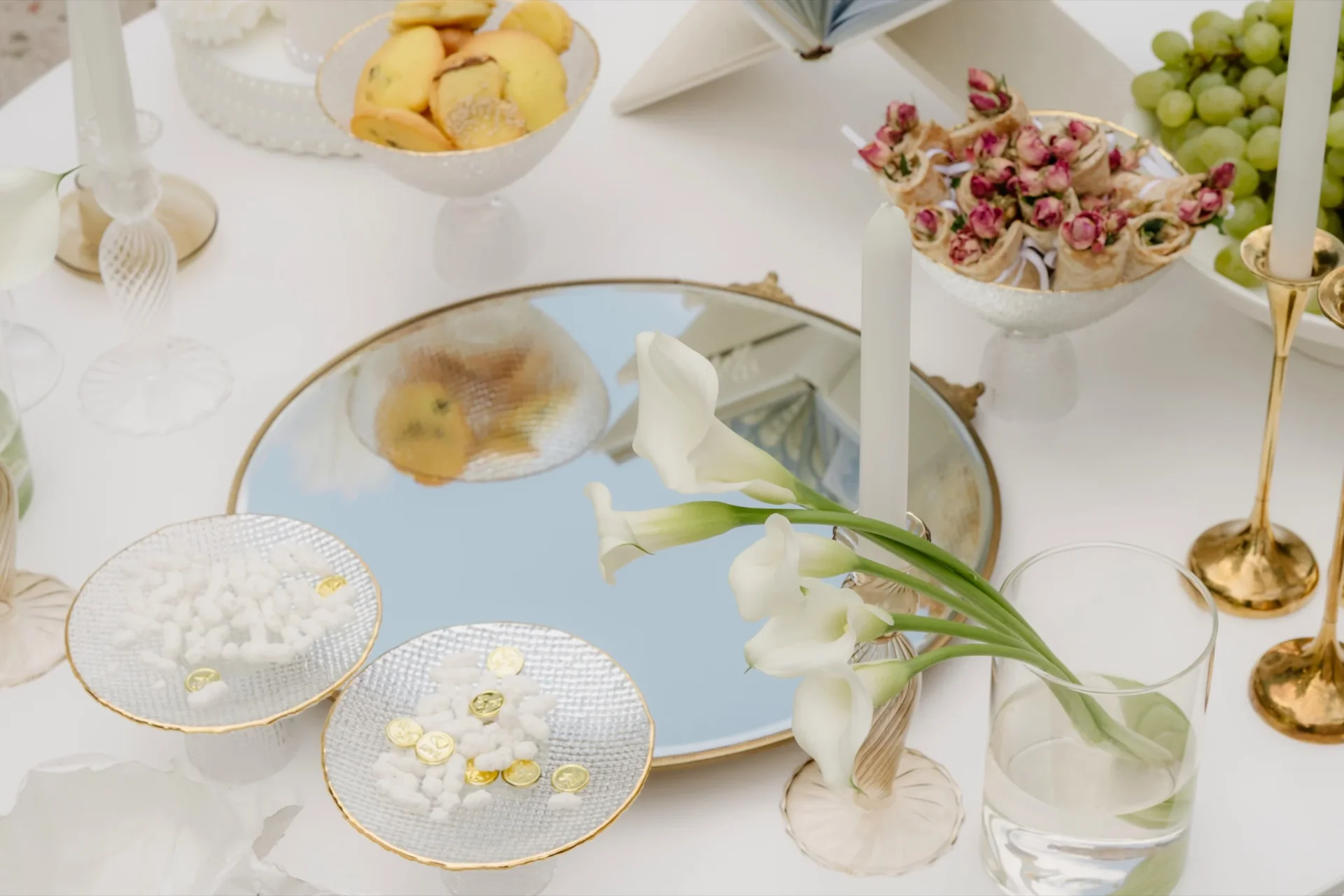 Table setting with gold-rimmed glass dishes, candles, calla lily and sweets