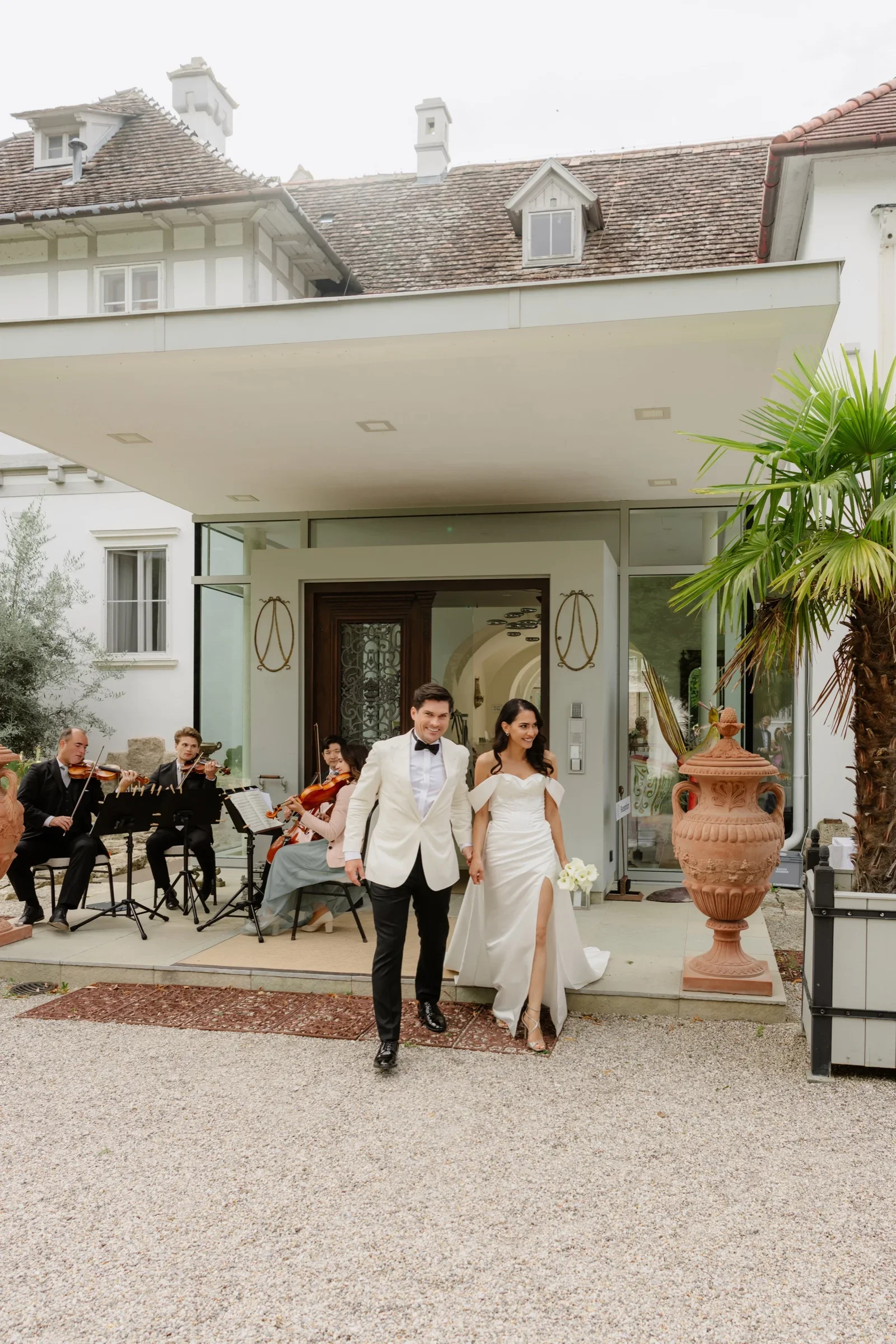 Bride and groom walking out of the villa entrance toward their guests