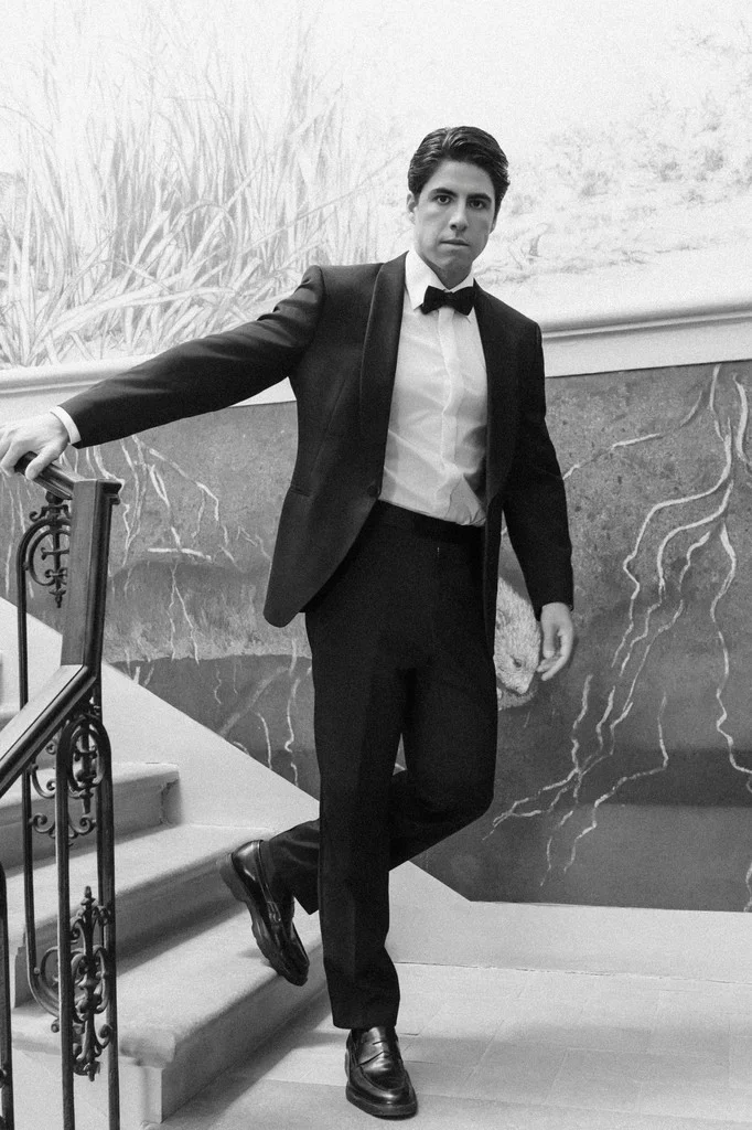 Groom in a tuxedo leaning against an iron stair railing