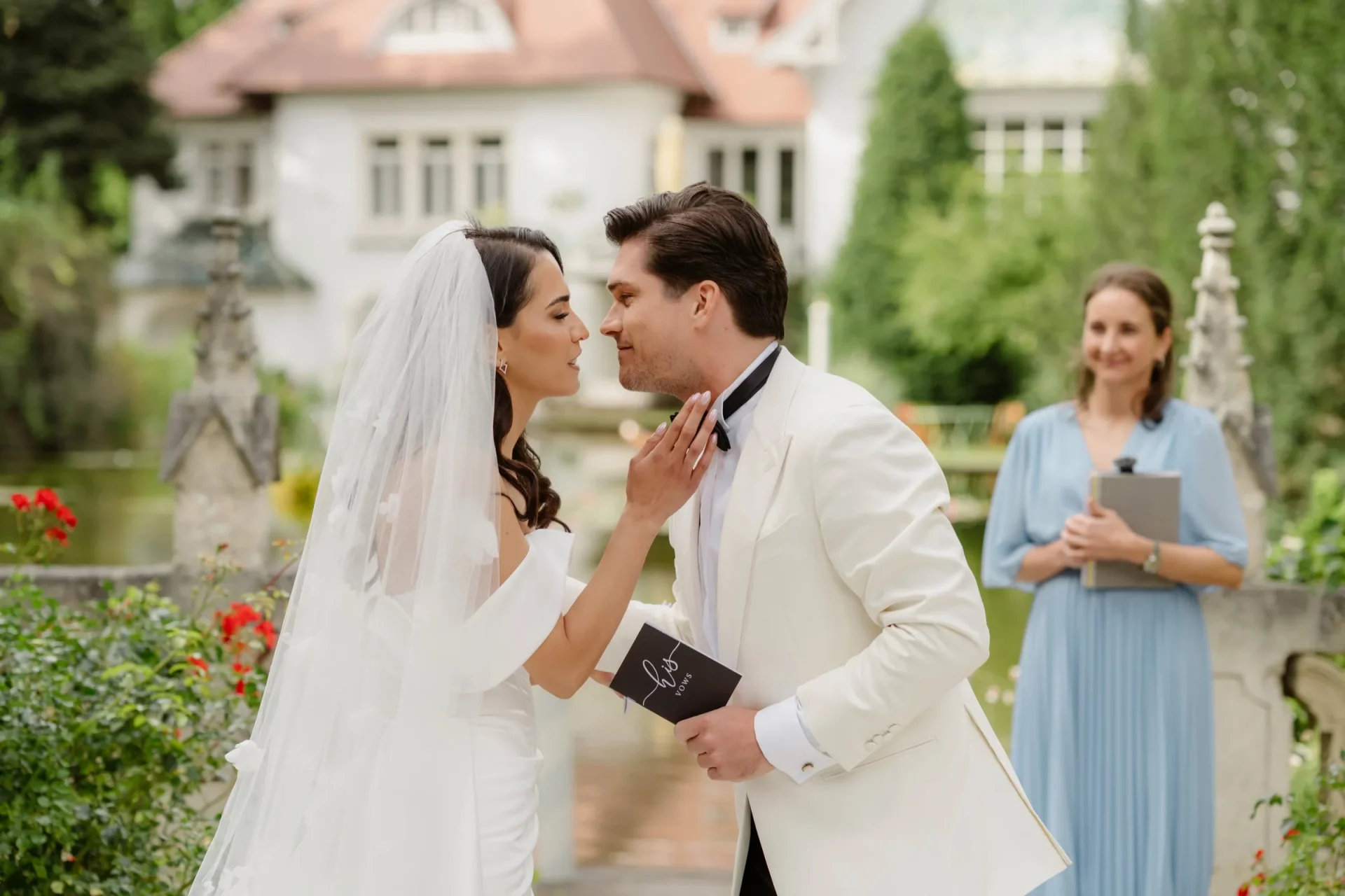 Bride and groom about to kiss in a rose garden while a woman in blue looks on