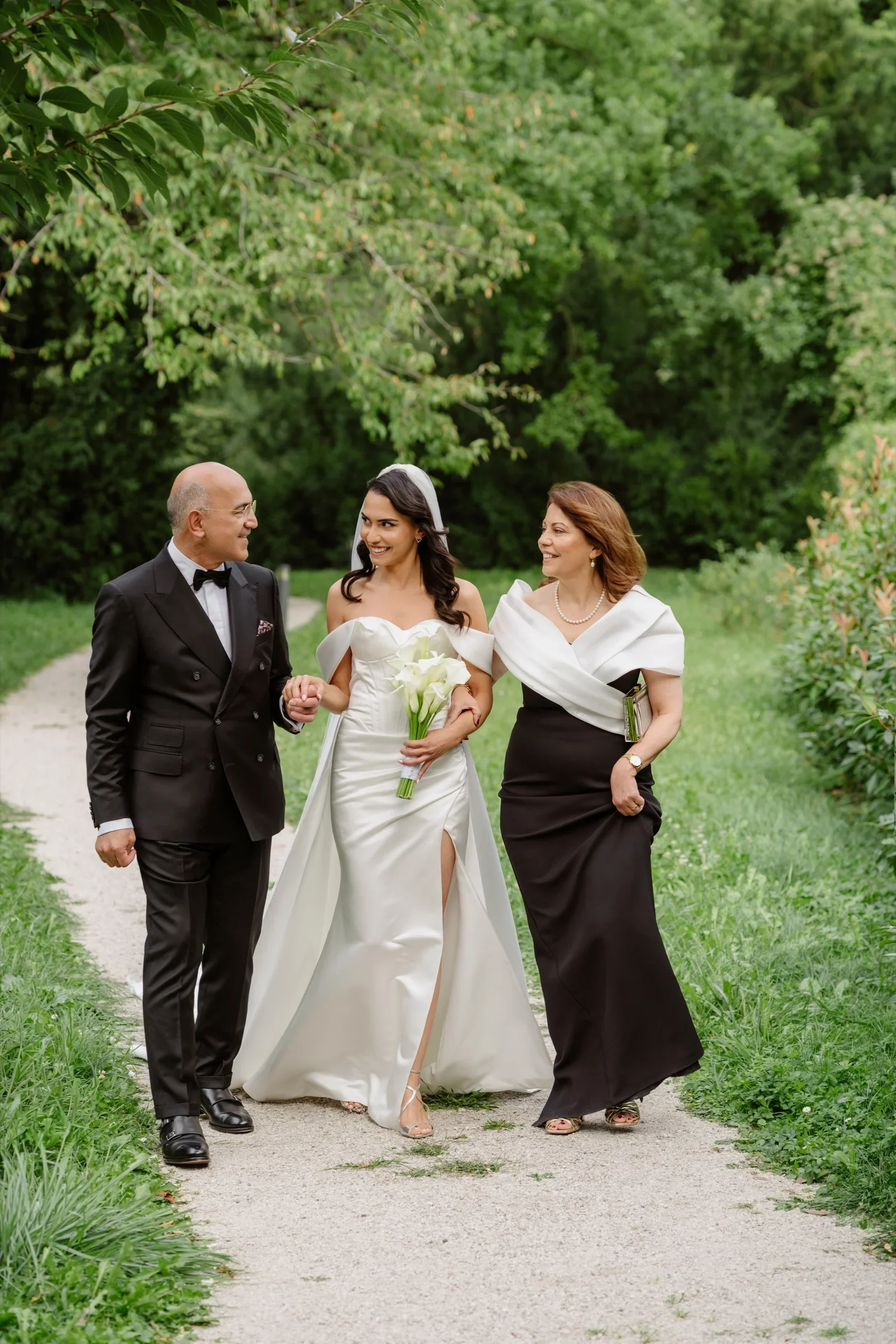 Bride in a white gown walking down the path with two companions in black