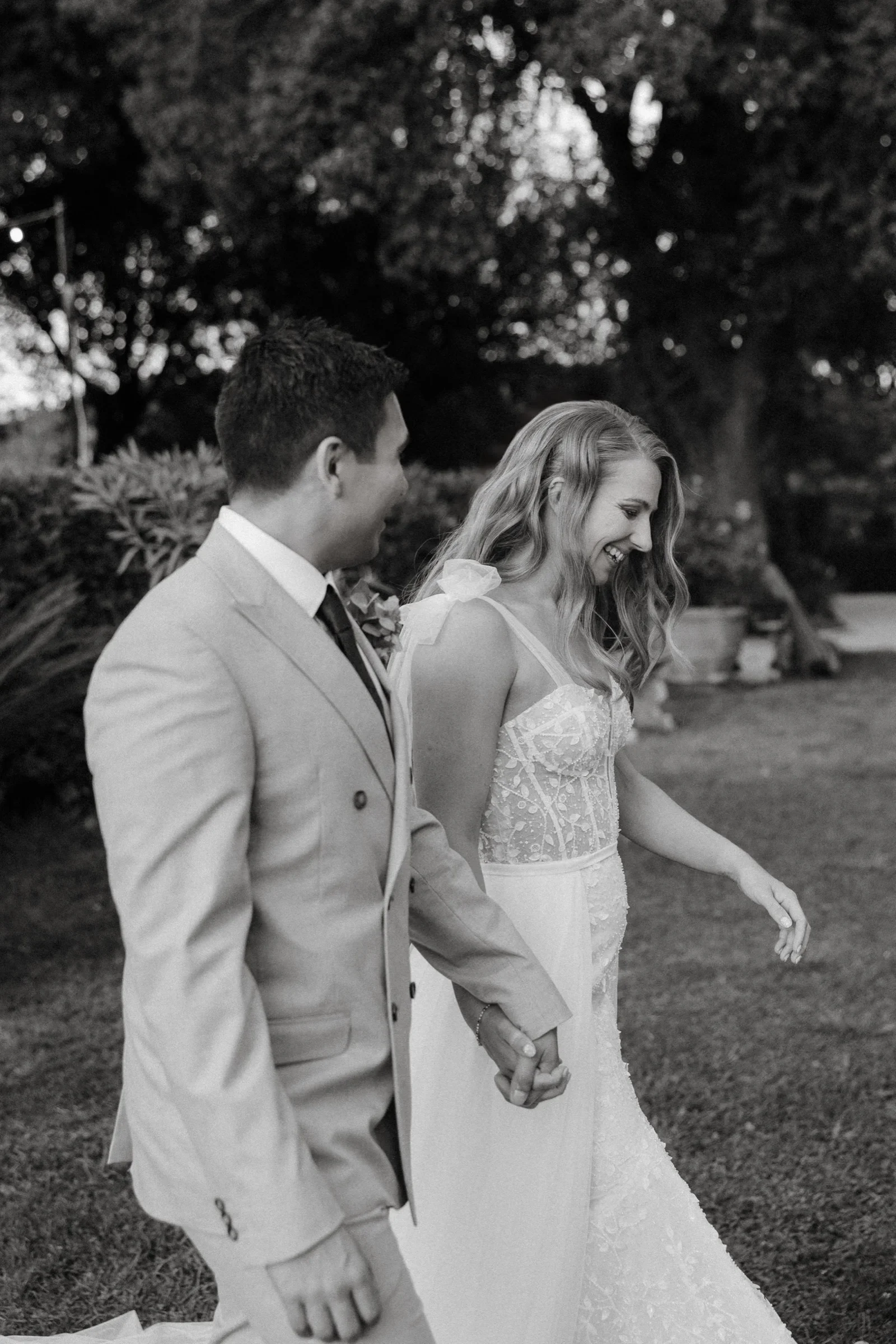 Black and white: the bride and groom walking hand in hand under the olive trees