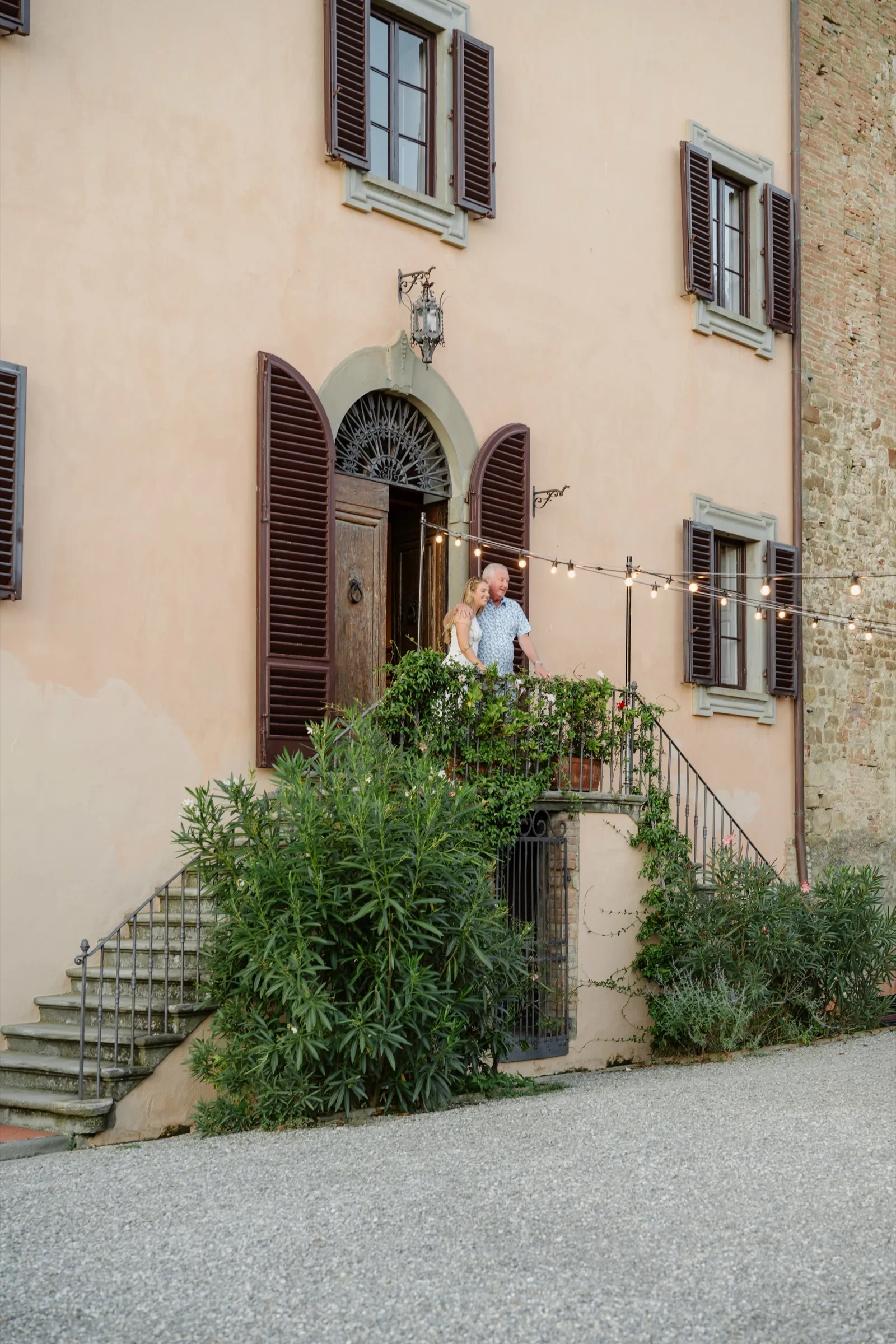 The groom stepping out of the villa's arched front door, framed by potted greenery
