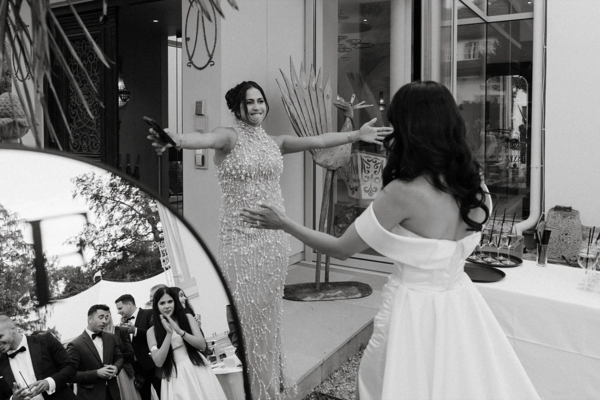 Black and white photo of the bride and a guest in a sparkling gown opening their arms to hug
