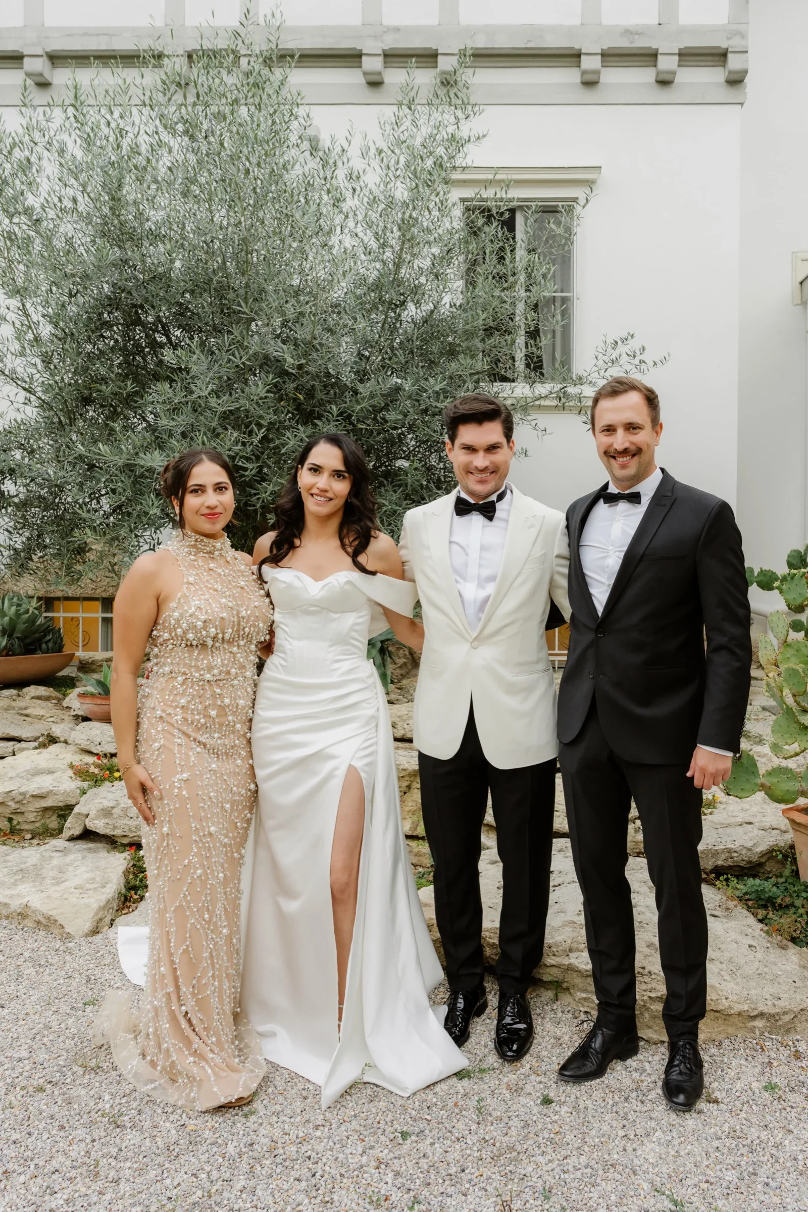 Bride and groom posing with two guests in front of an olive tree