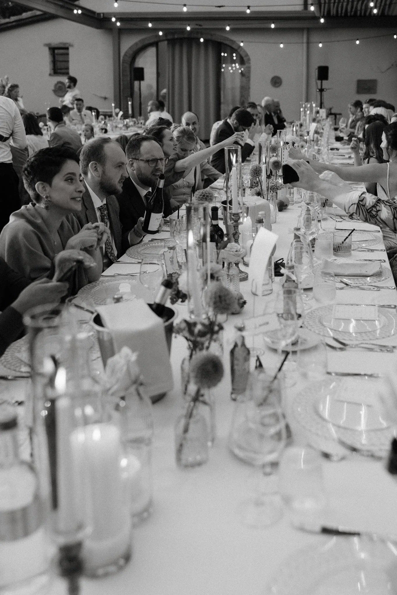 Black and white view along the long dinner table, guests talking over candlelight