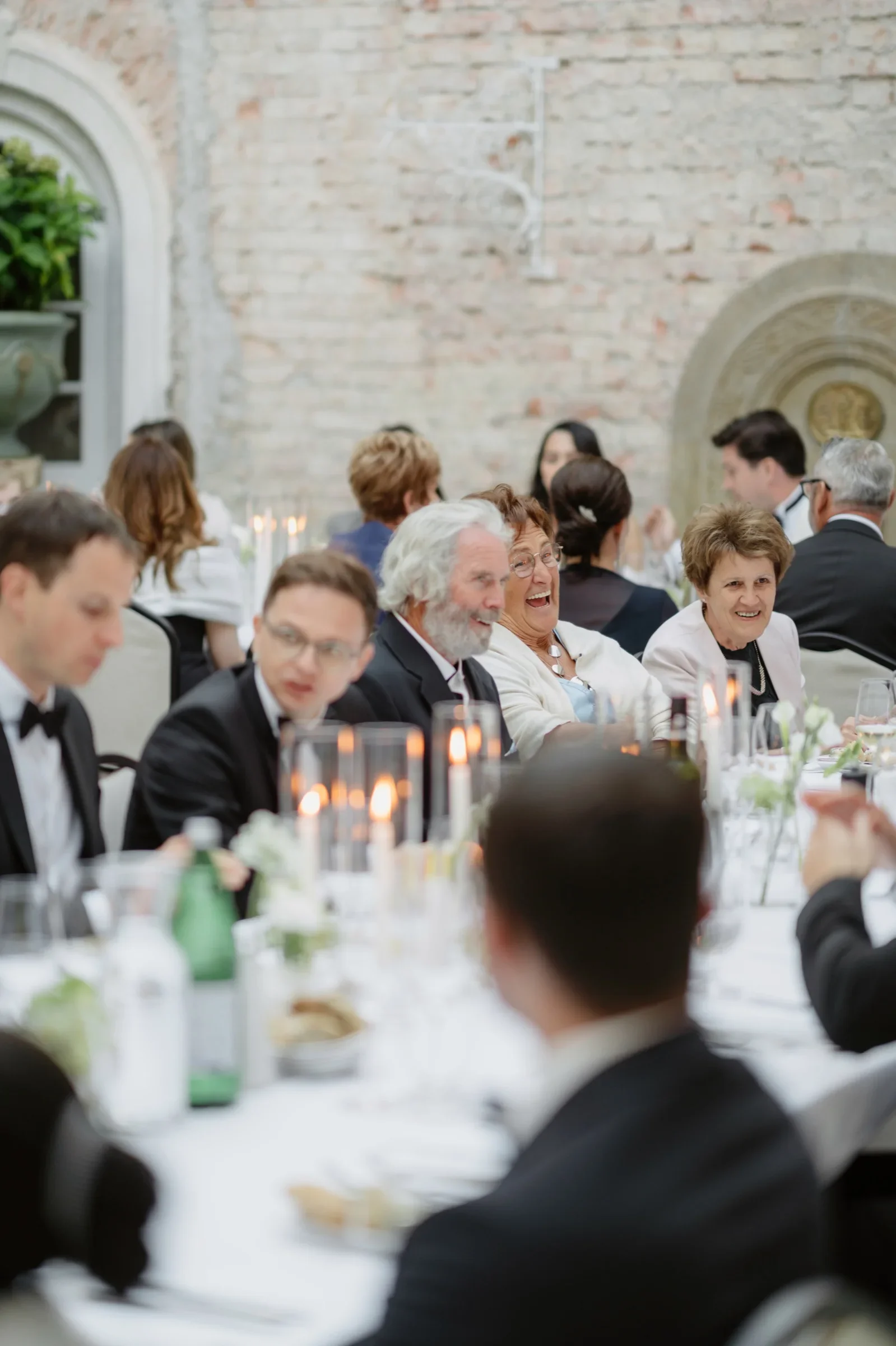 Wedding guests in black tie seated and chatting at candlelit dinner tables