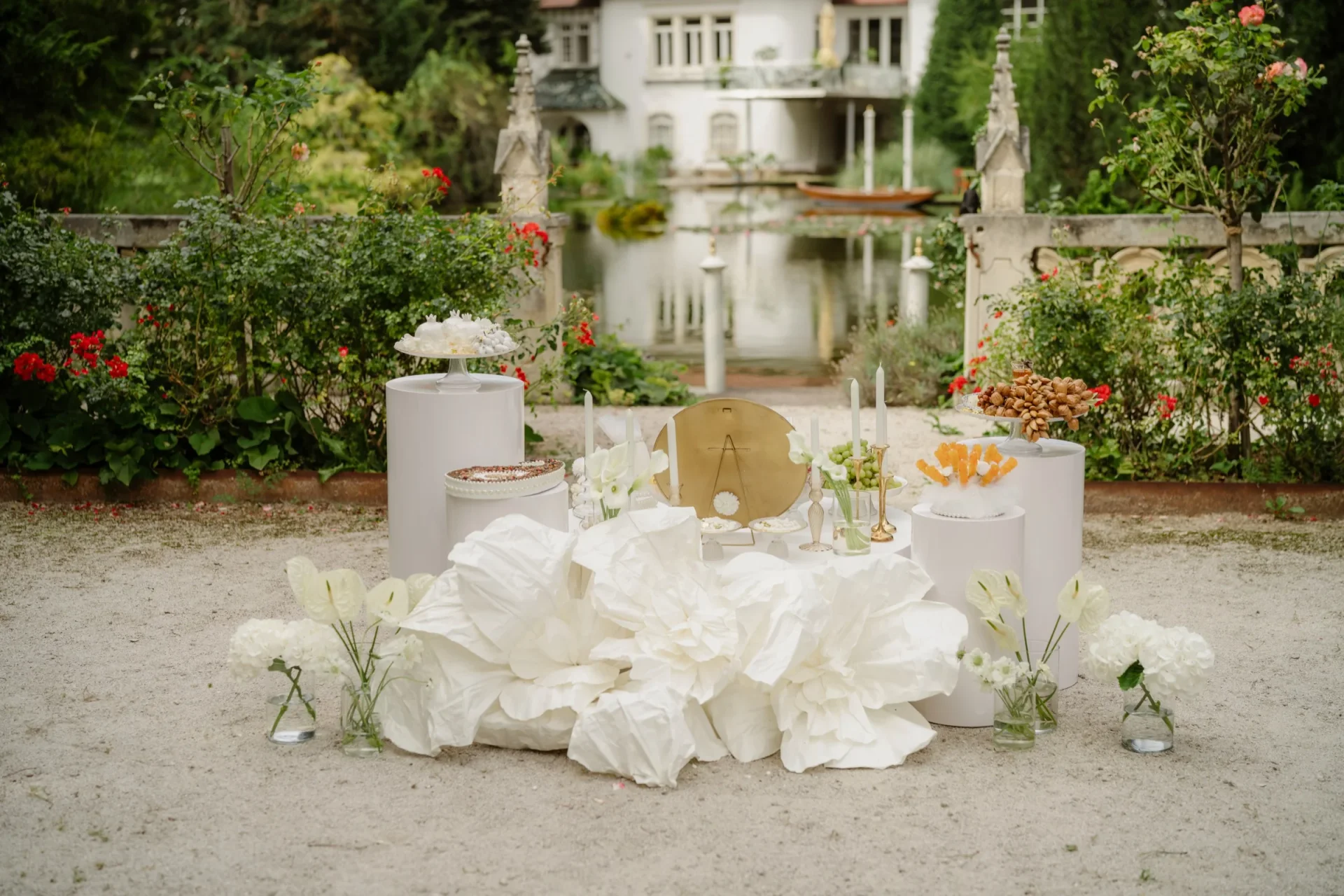 Ceremony arrangement of large white paper flowers and roses on a gravel courtyard