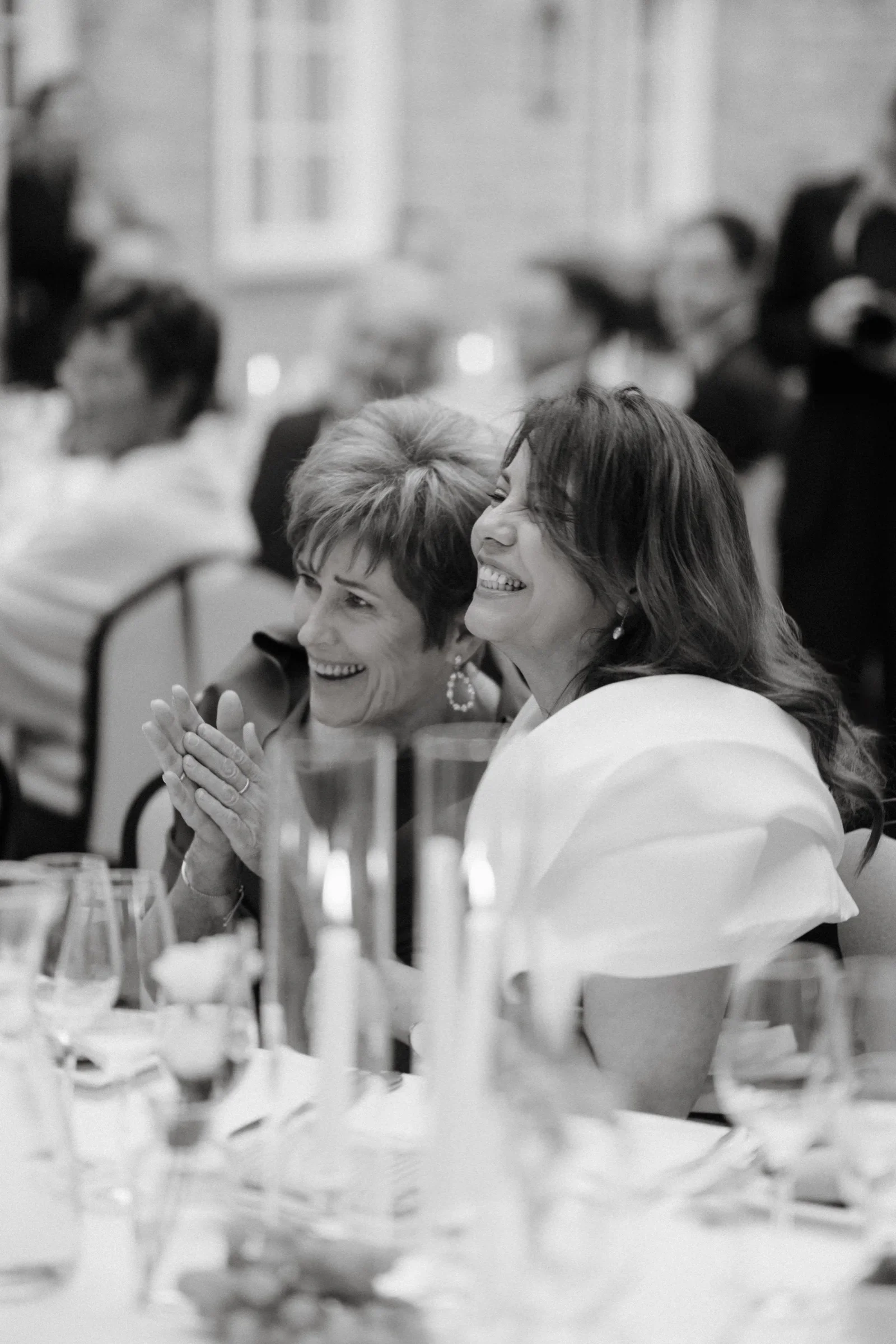 Two guests laughing together at the dinner table, black and white