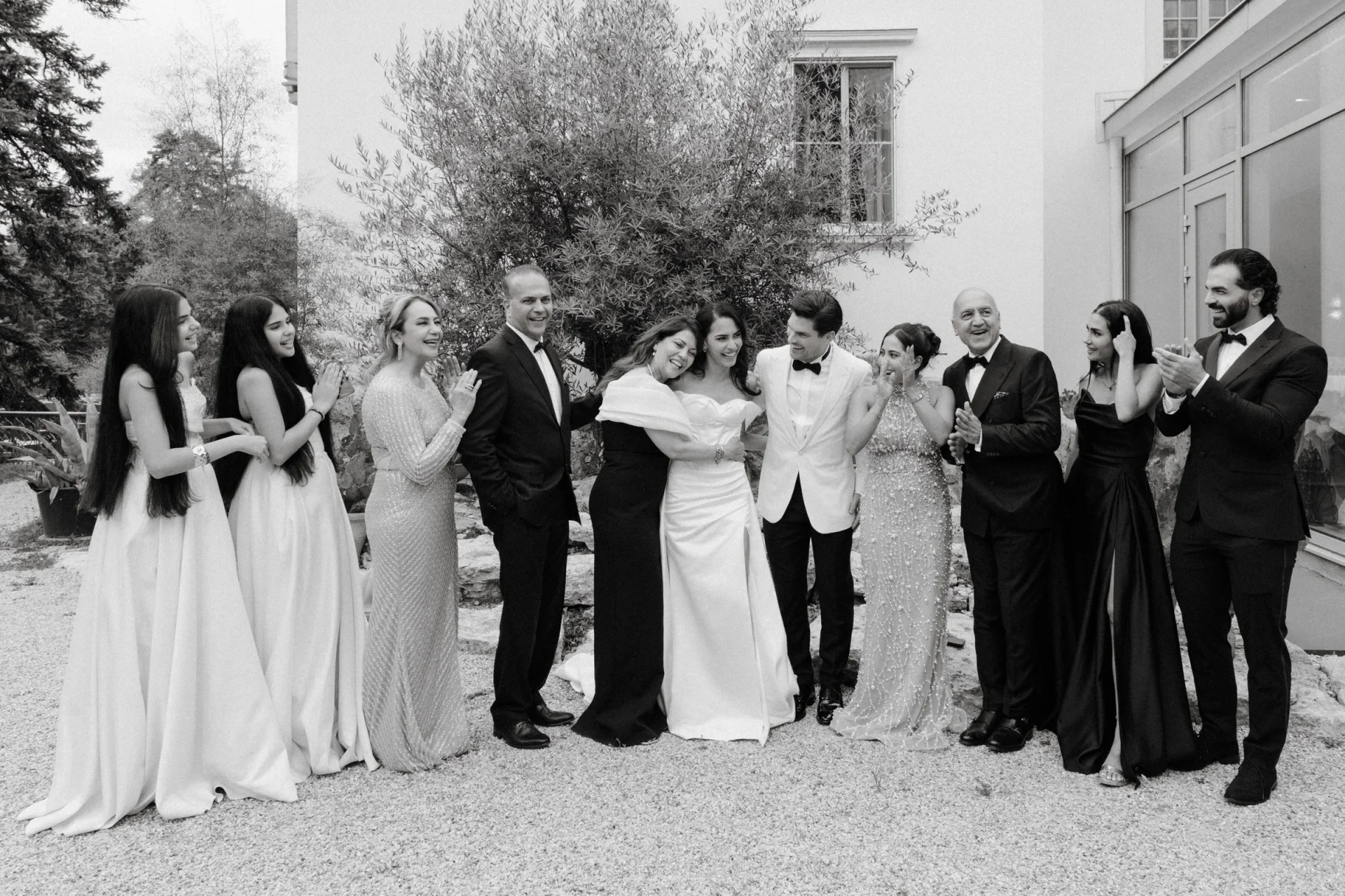 Large wedding party laughing together in a courtyard, black and white