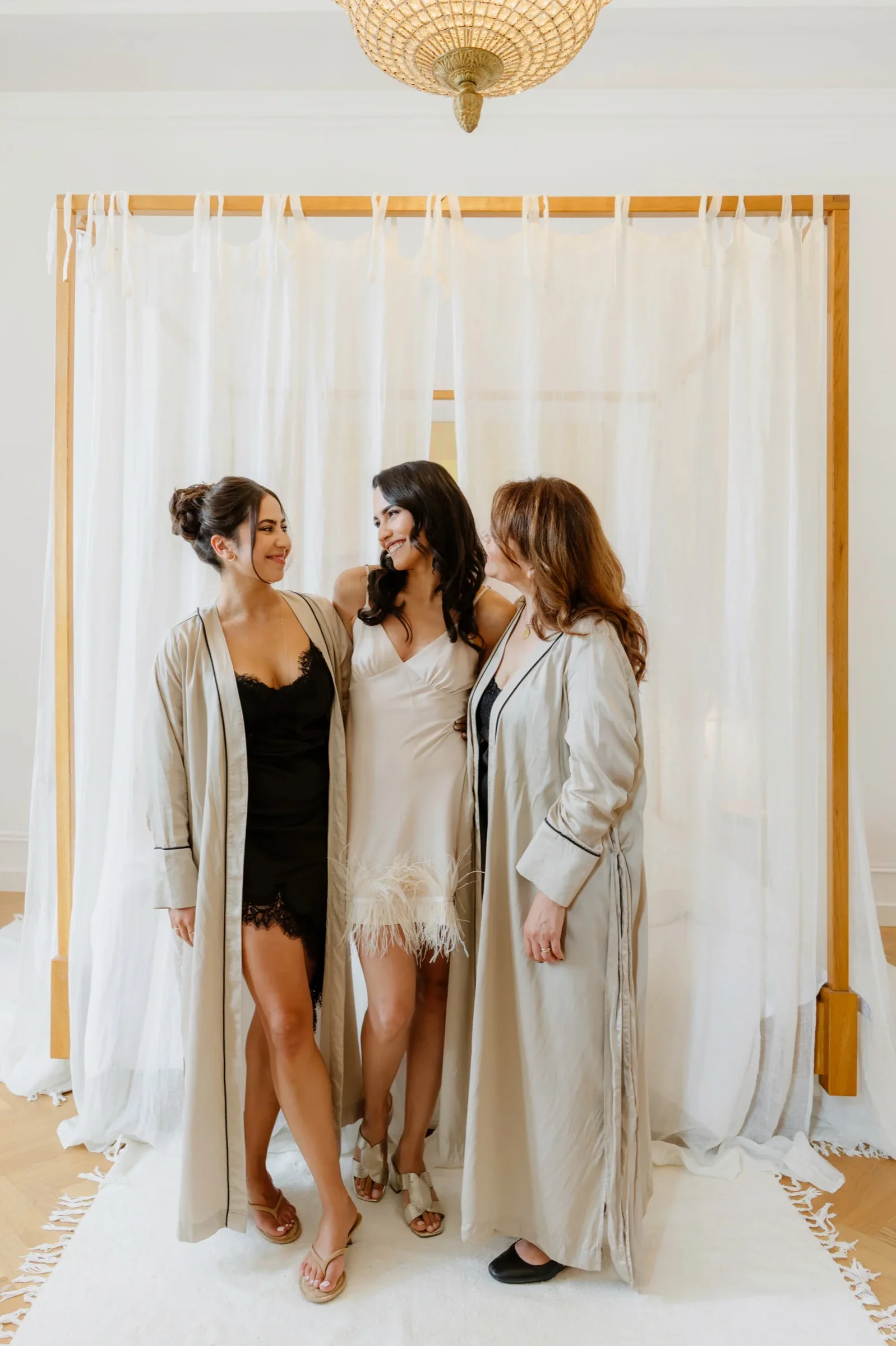 Bride and two bridesmaids in robes standing before a draped gold frame