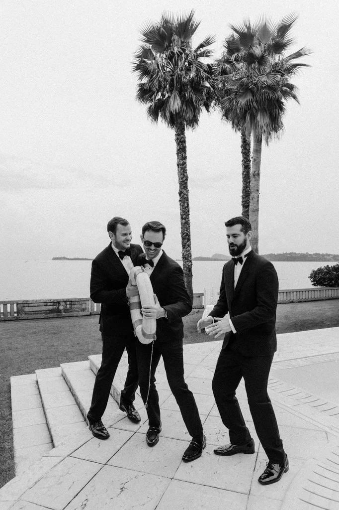 Groomsmen carrying the groom down steps beneath tall palm trees