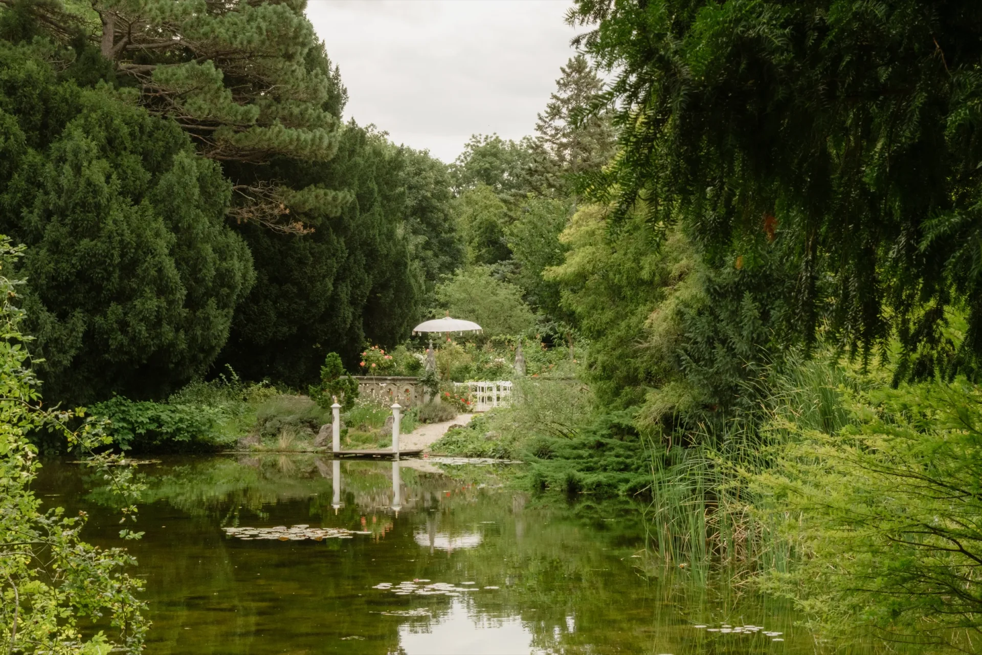 Pond in the castle park with a small garden pavilion and a parasol on the far bank