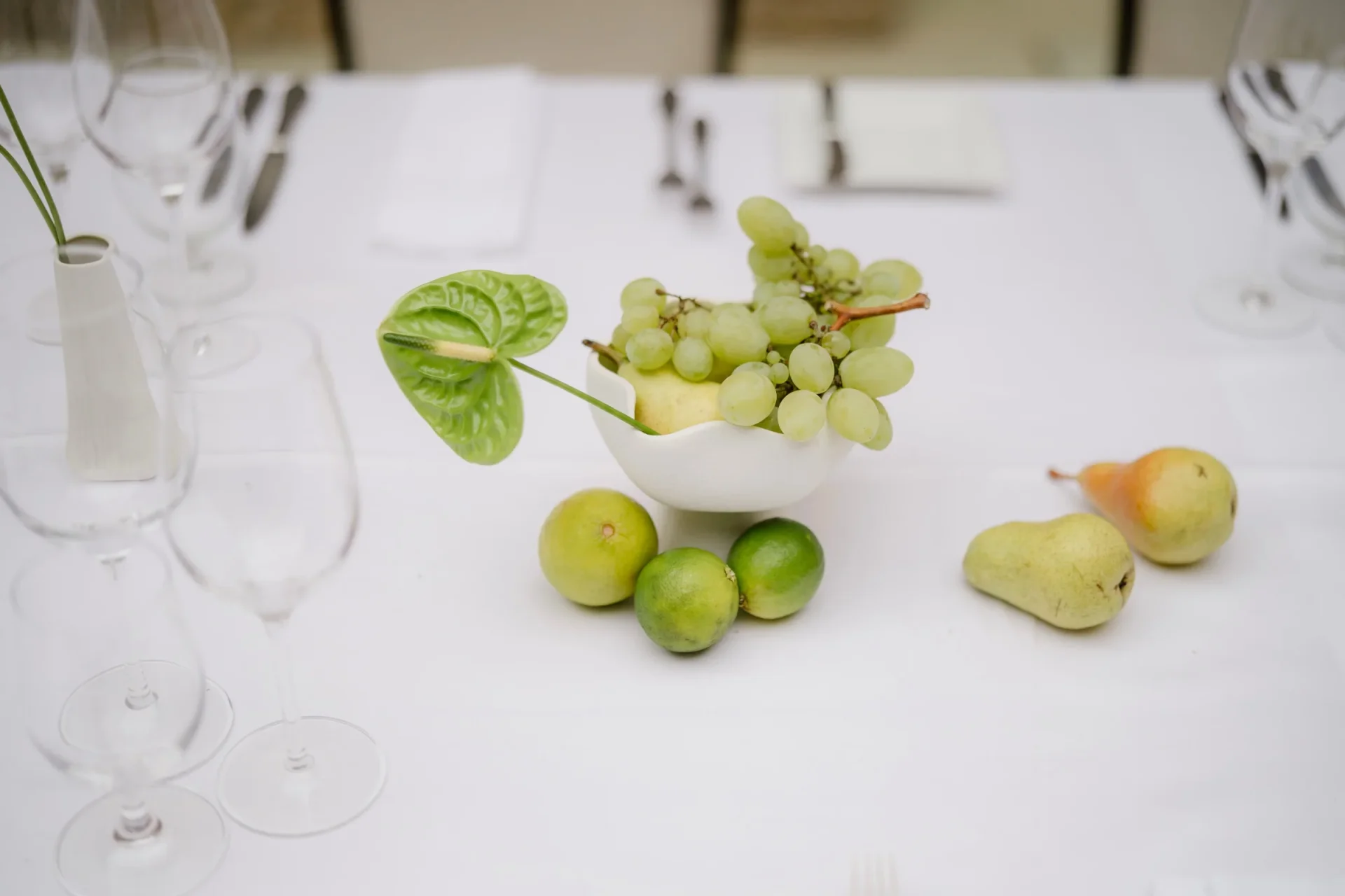 Table detail with a bowl of green grapes, limes and pears next to wine glasses