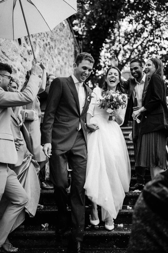 Newlyweds leaving the ceremony under umbrellas as guests cheer