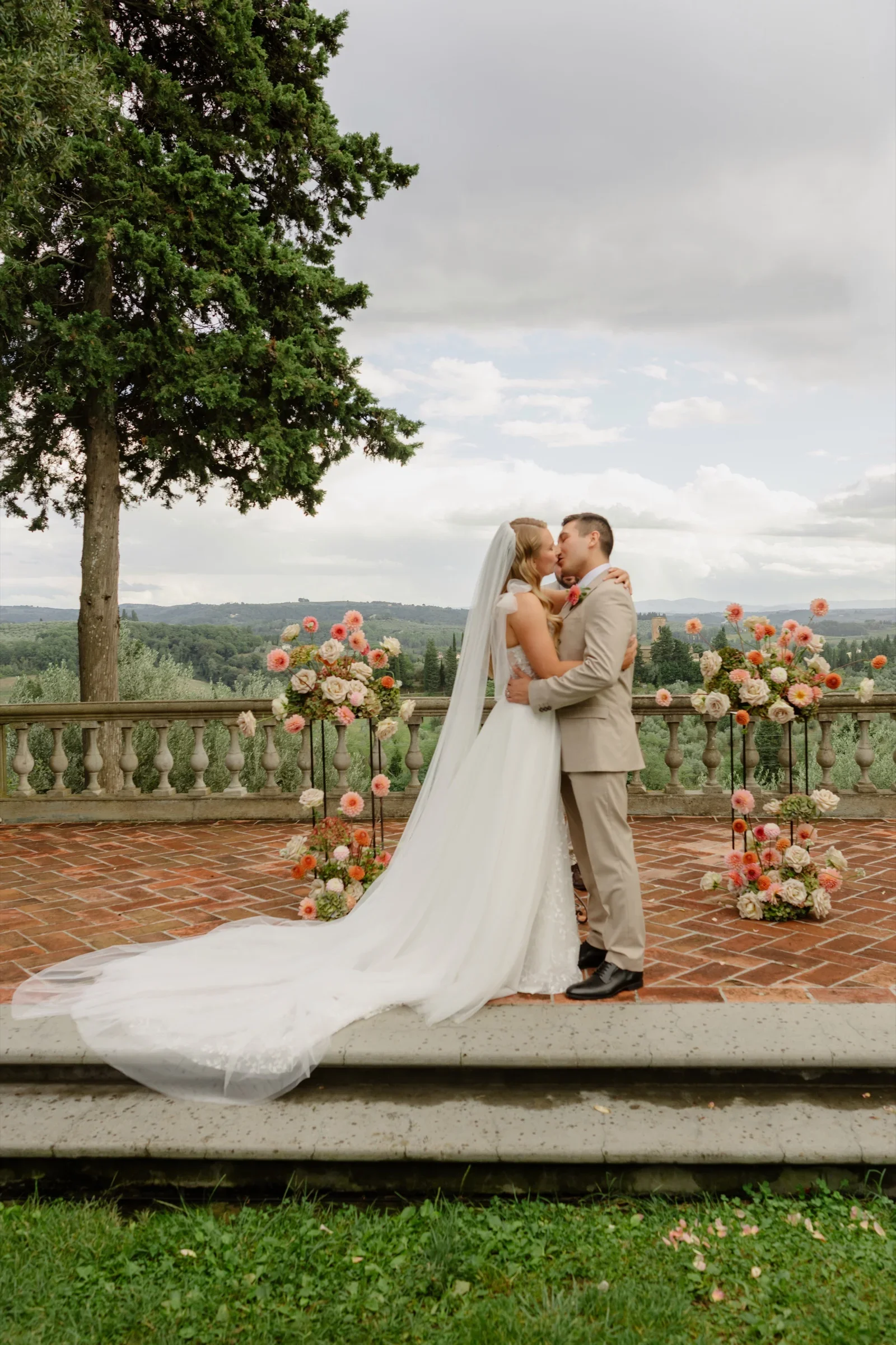 The couple's first kiss on the balustraded terrace, the bride's train spread across the stone