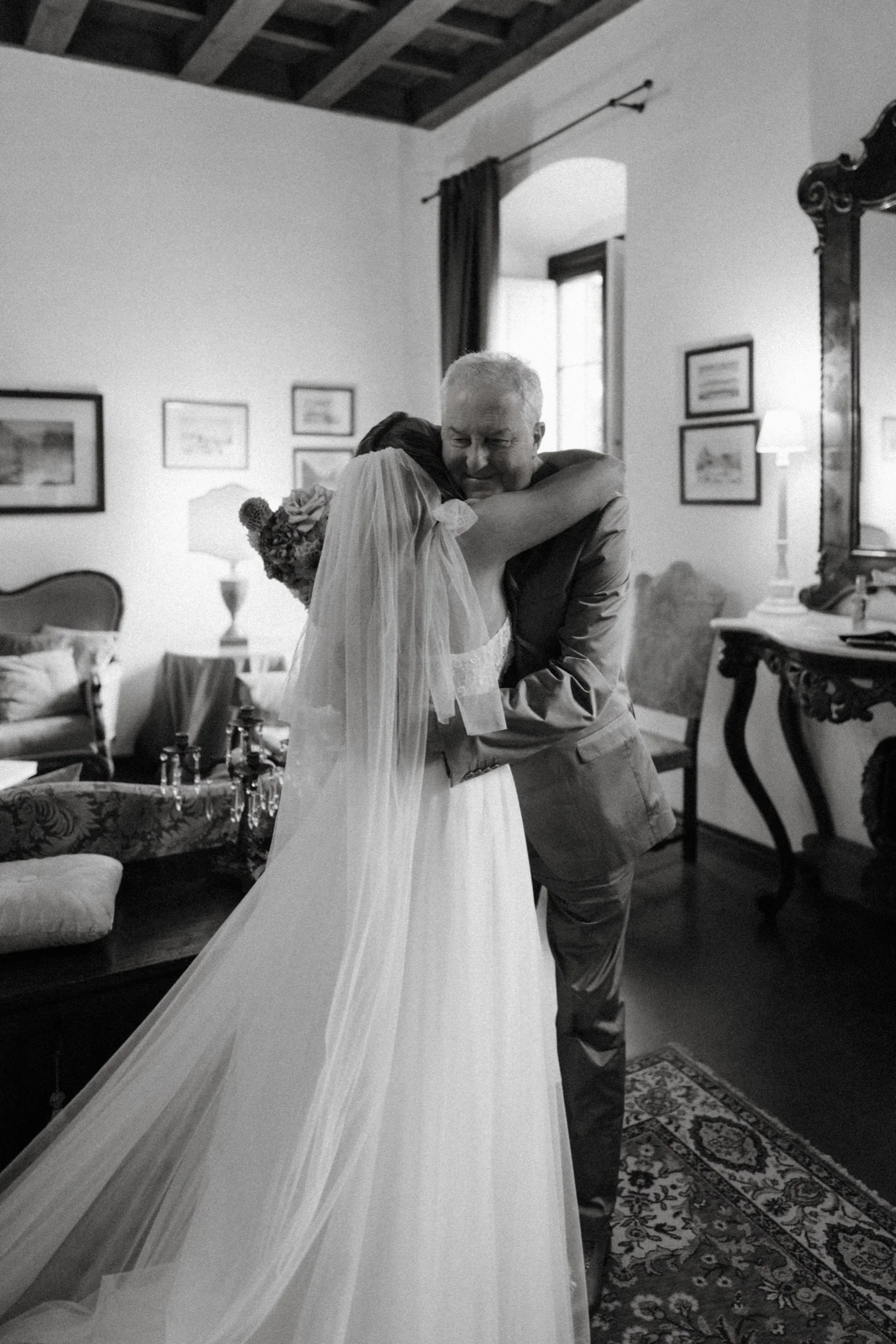 Black and white: the bride, veiled, embracing her father before the ceremony