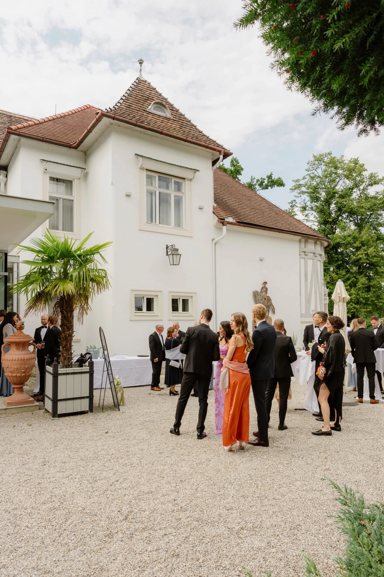 Wedding guests gathering in the courtyard of a white castle with a palm tree