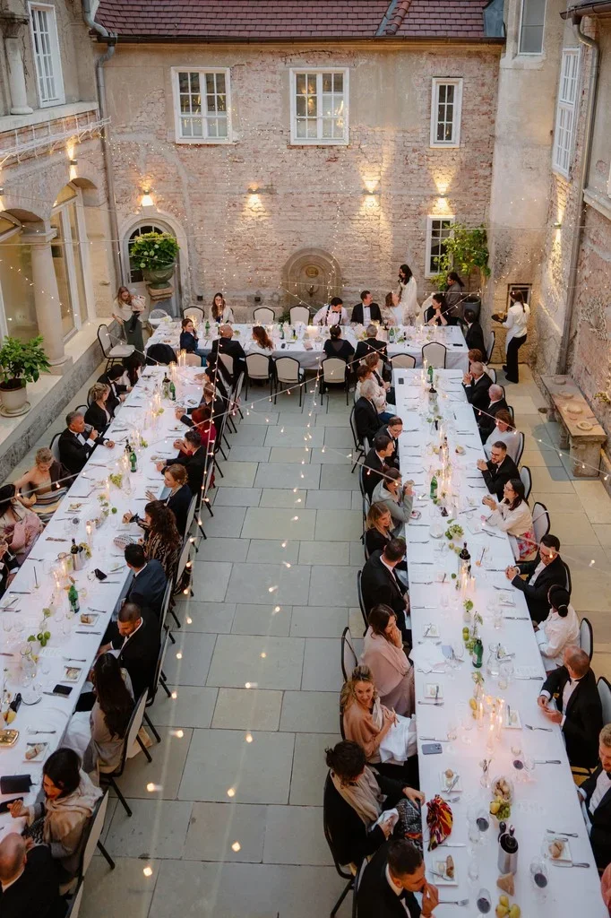 Guests dining at long tables in a candlelit stone courtyard