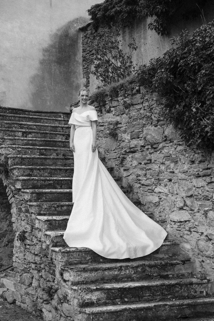 Bride standing on weathered stone steps beside an old wall