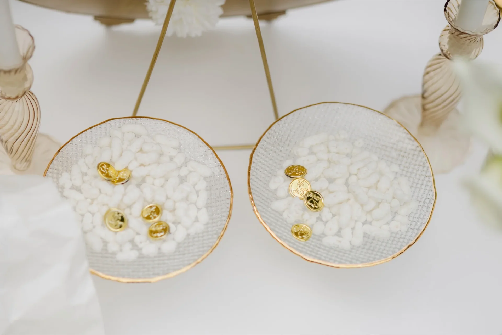 Two gold-rimmed glass bowls with white sugar and gold coins on a styled table