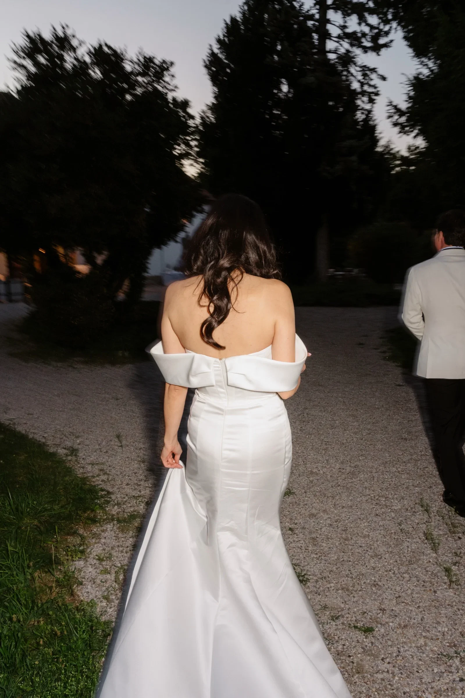 Bride in an off-shoulder gown seen from behind on a garden path