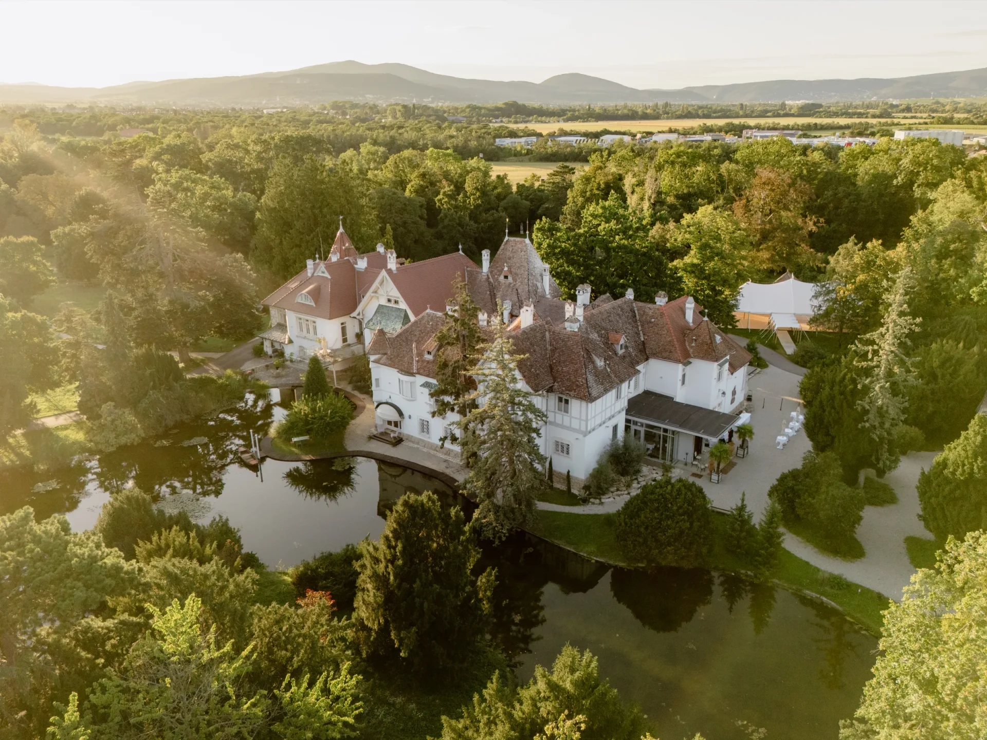 Aerial view of Schoenau Castle surrounded by park, pond and wooded hills in golden light