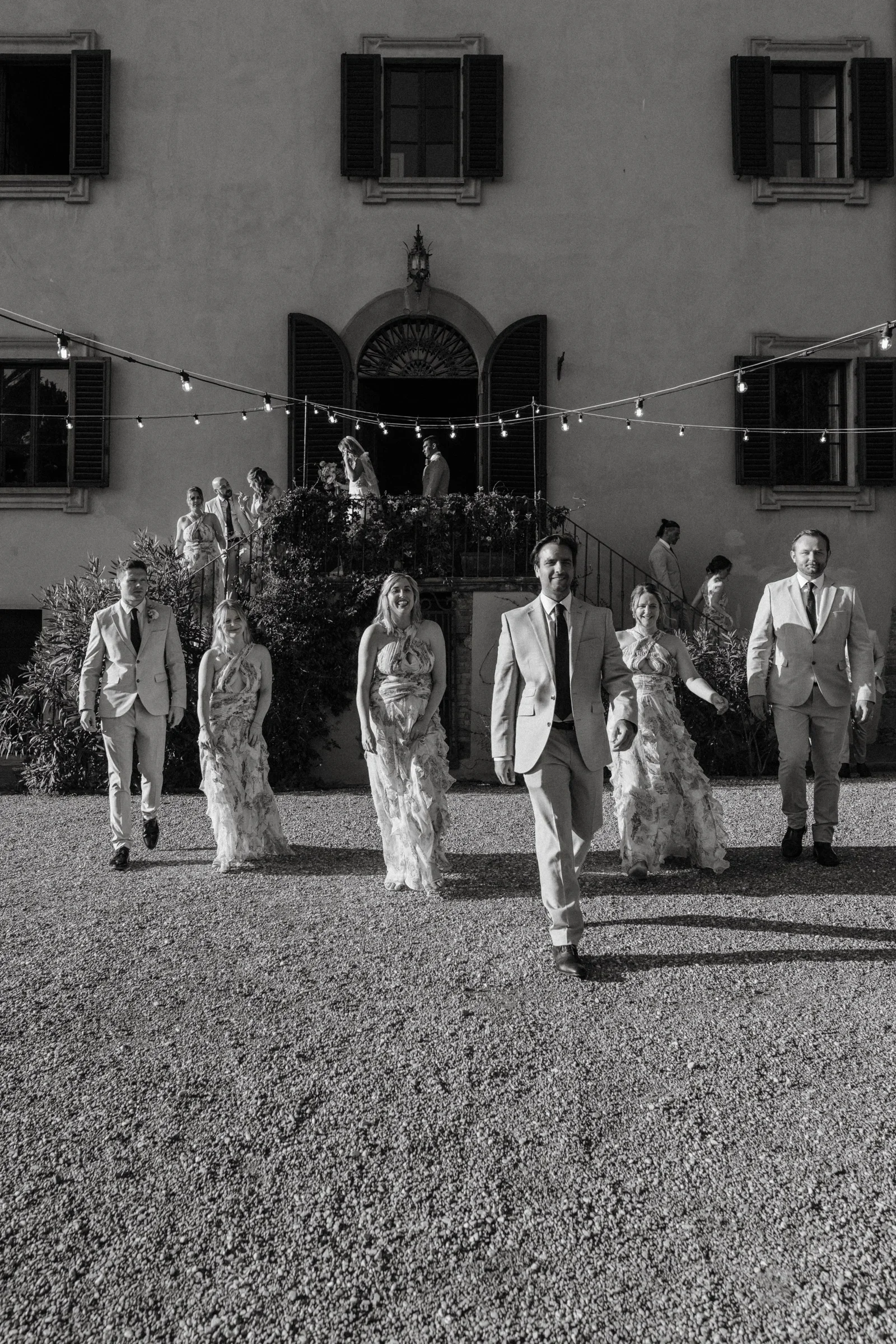 Black and white: the wedding party walking across the courtyard towards the villa