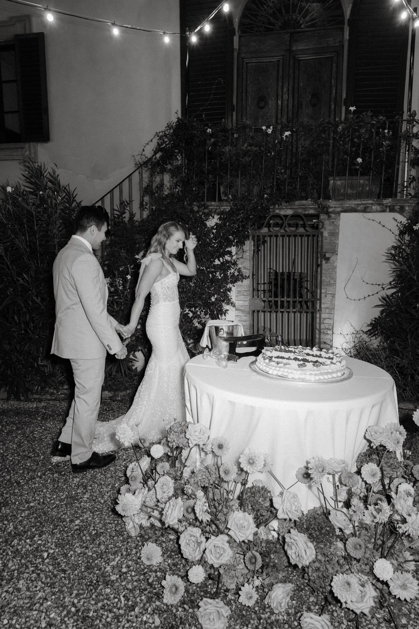 Black and white: the couple at the flower-ringed cake table at night