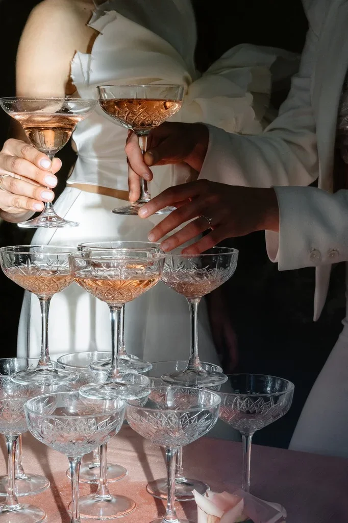 Hands lifting coupes from a stacked champagne glass tower